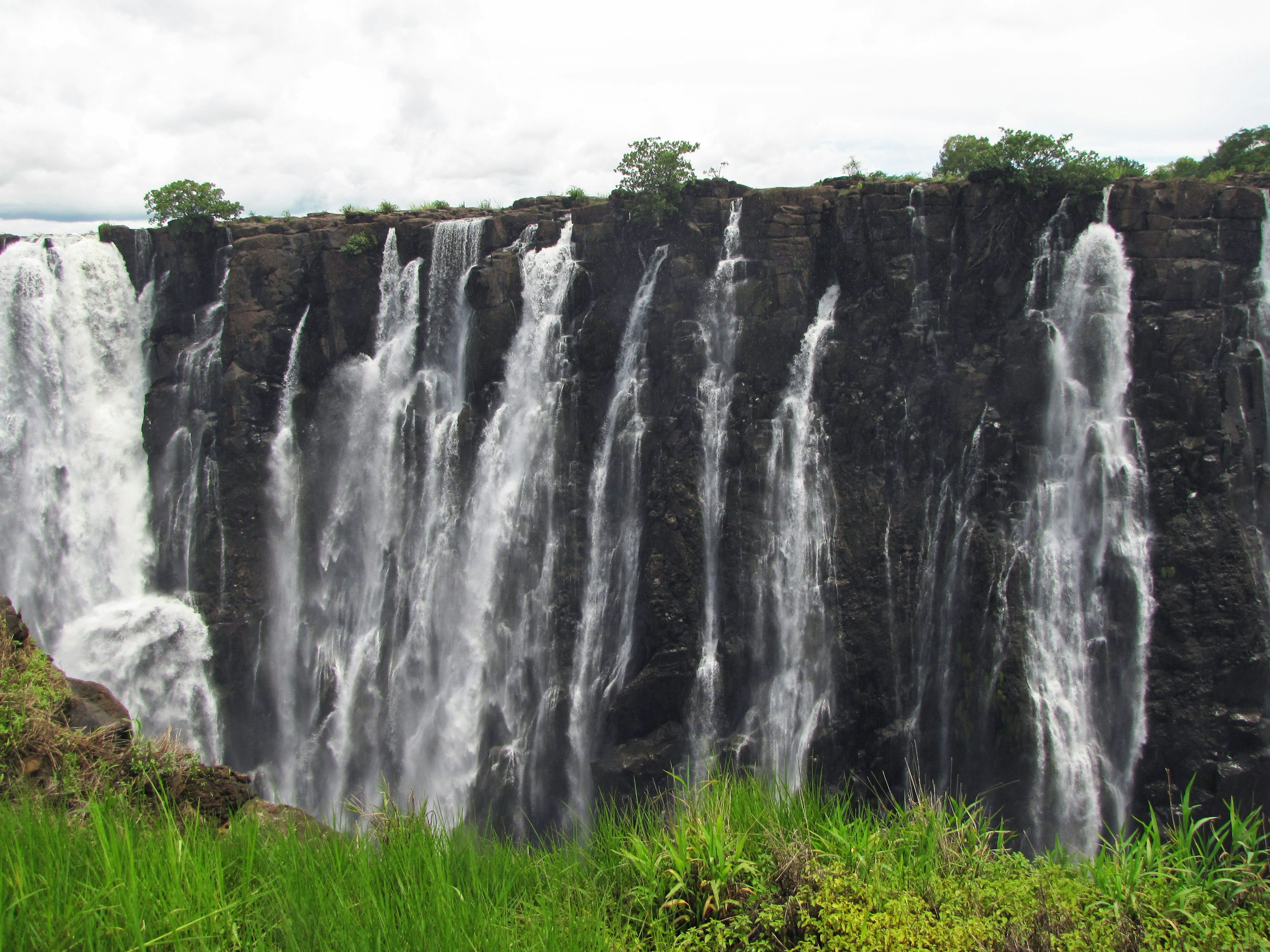 A stunning view of waterfalls cascading down rocky cliffs with lush green grass