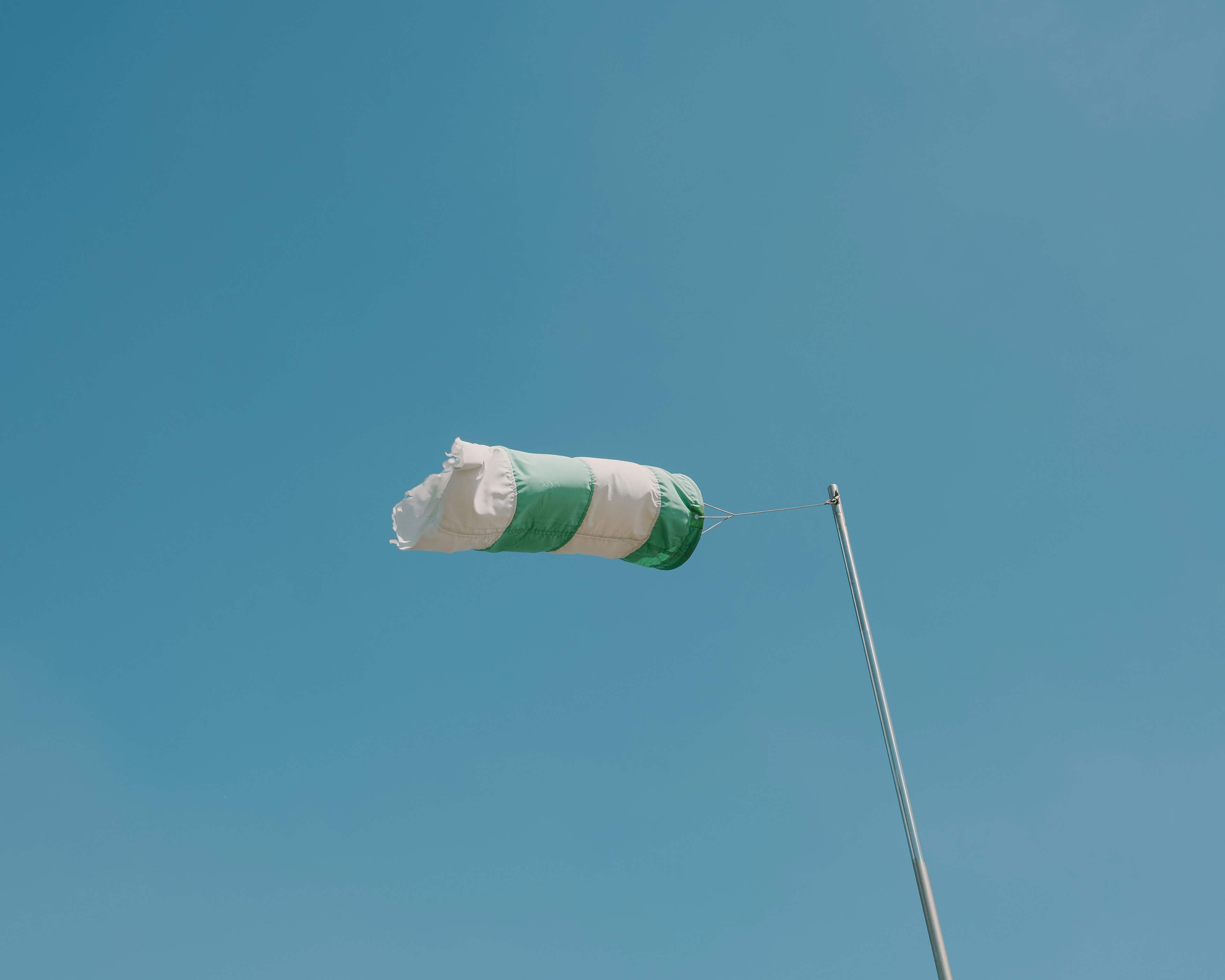 Green and white windsock swaying against a blue sky