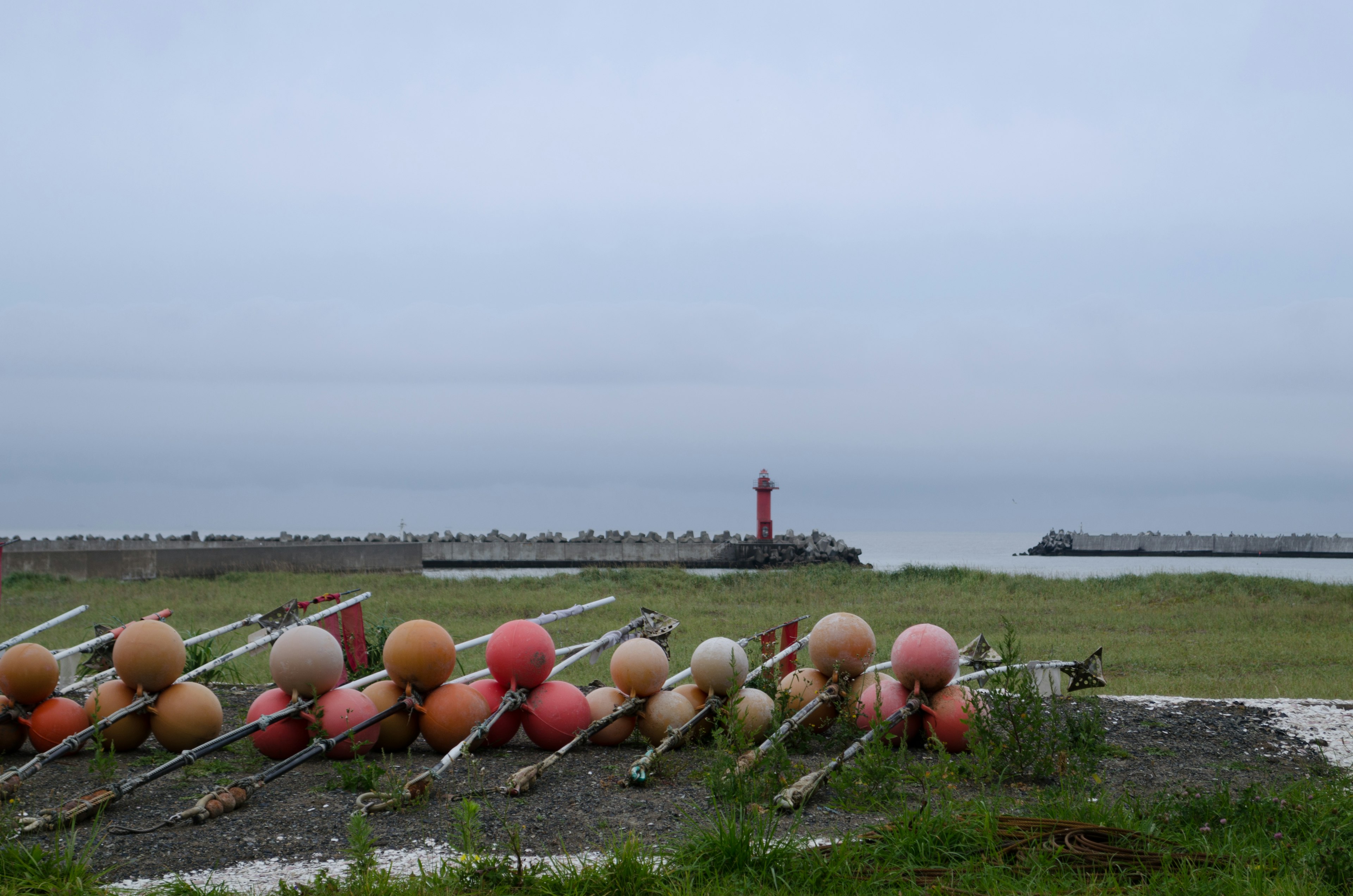 Buoys arranged on the shore with a red lighthouse in the background