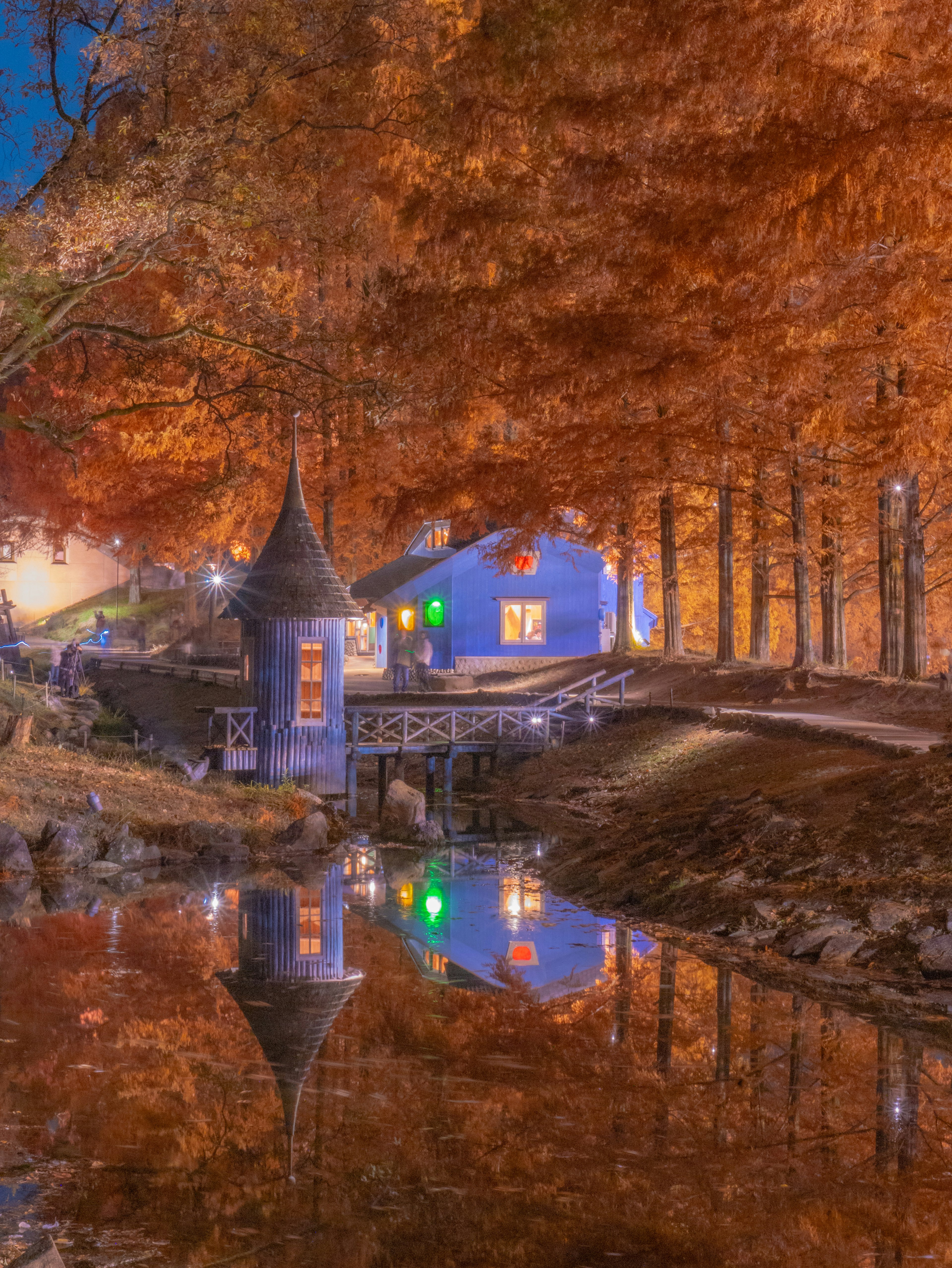 Ruhige Szene eines blauen Hauses und orangefarbenen Bäumen, die sich in einem ruhigen Fluss spiegeln