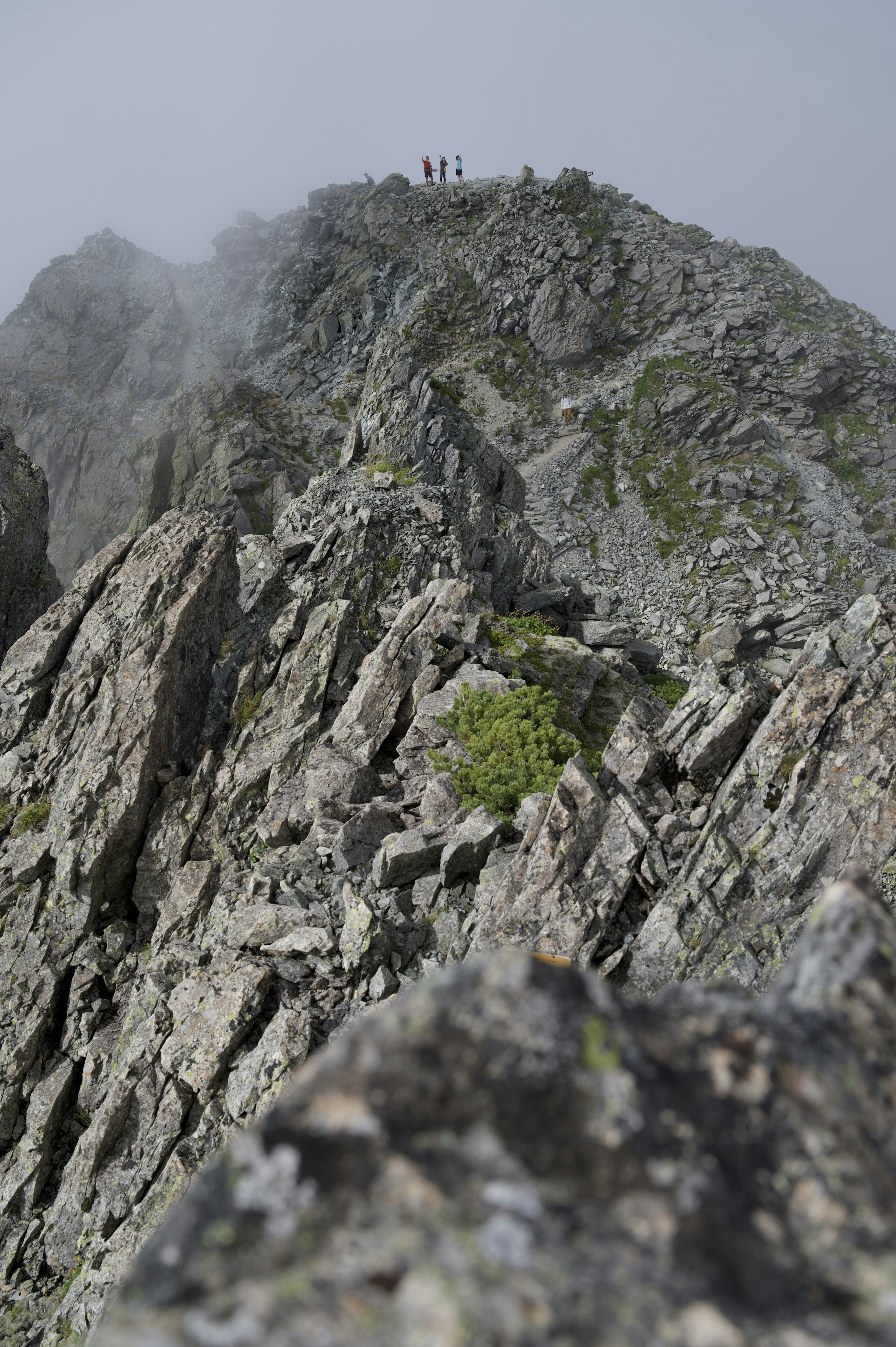 Personas de pie en la cima de una montaña rodeada de niebla y rocas