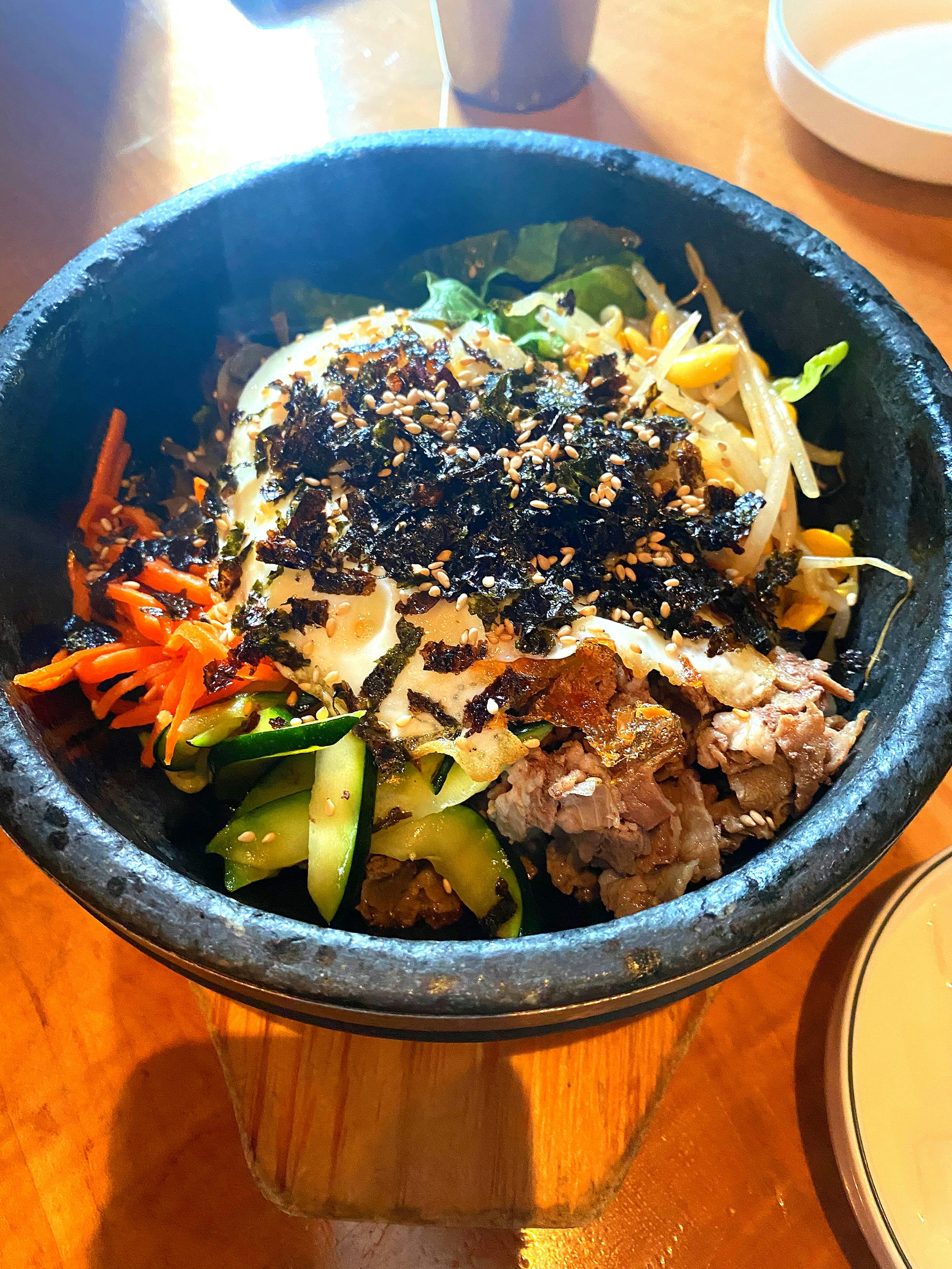 A stone bowl filled with bibimbap featuring colorful vegetables and meat