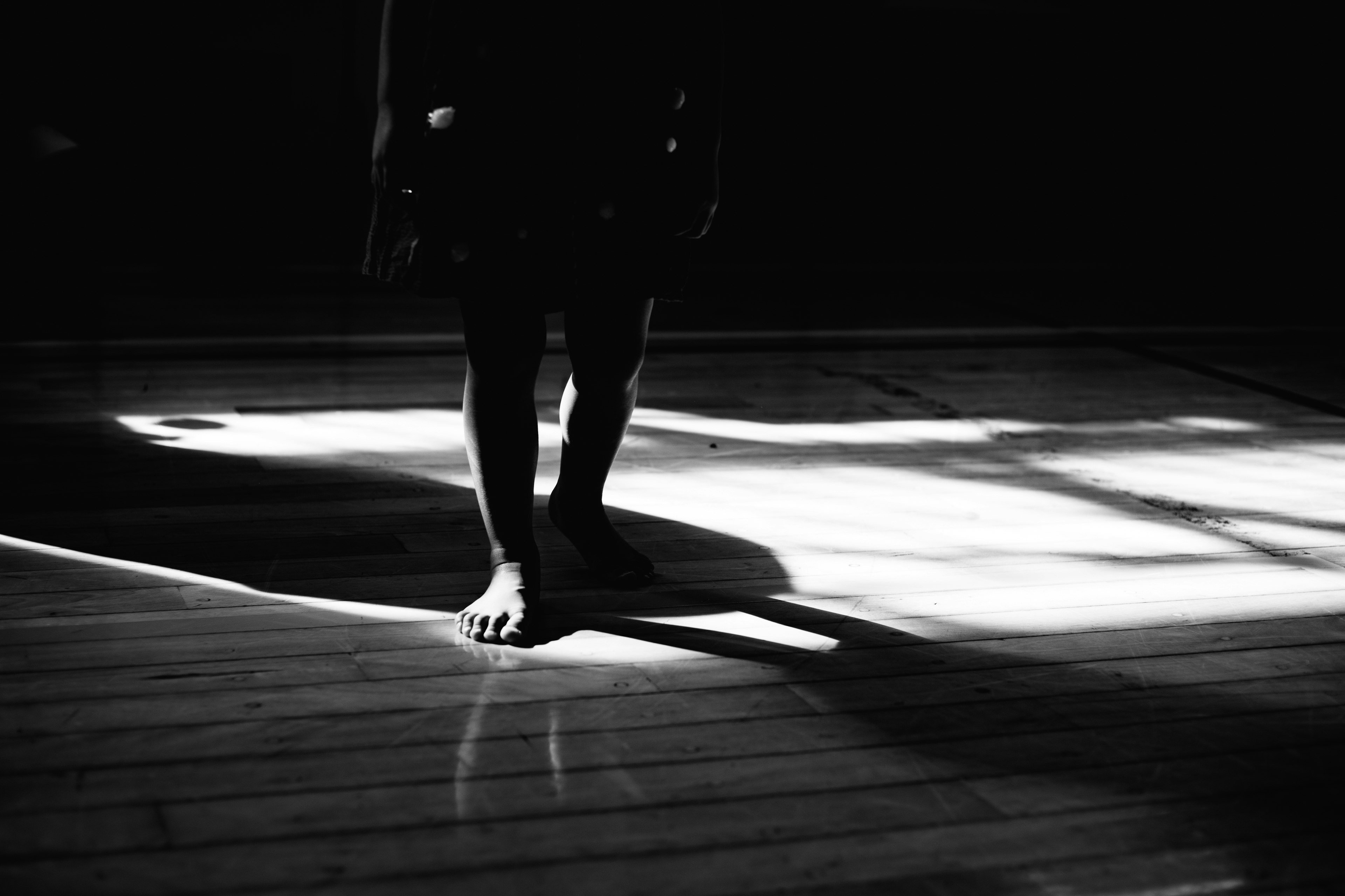 A child's feet standing on a wooden floor with dramatic shadows and light