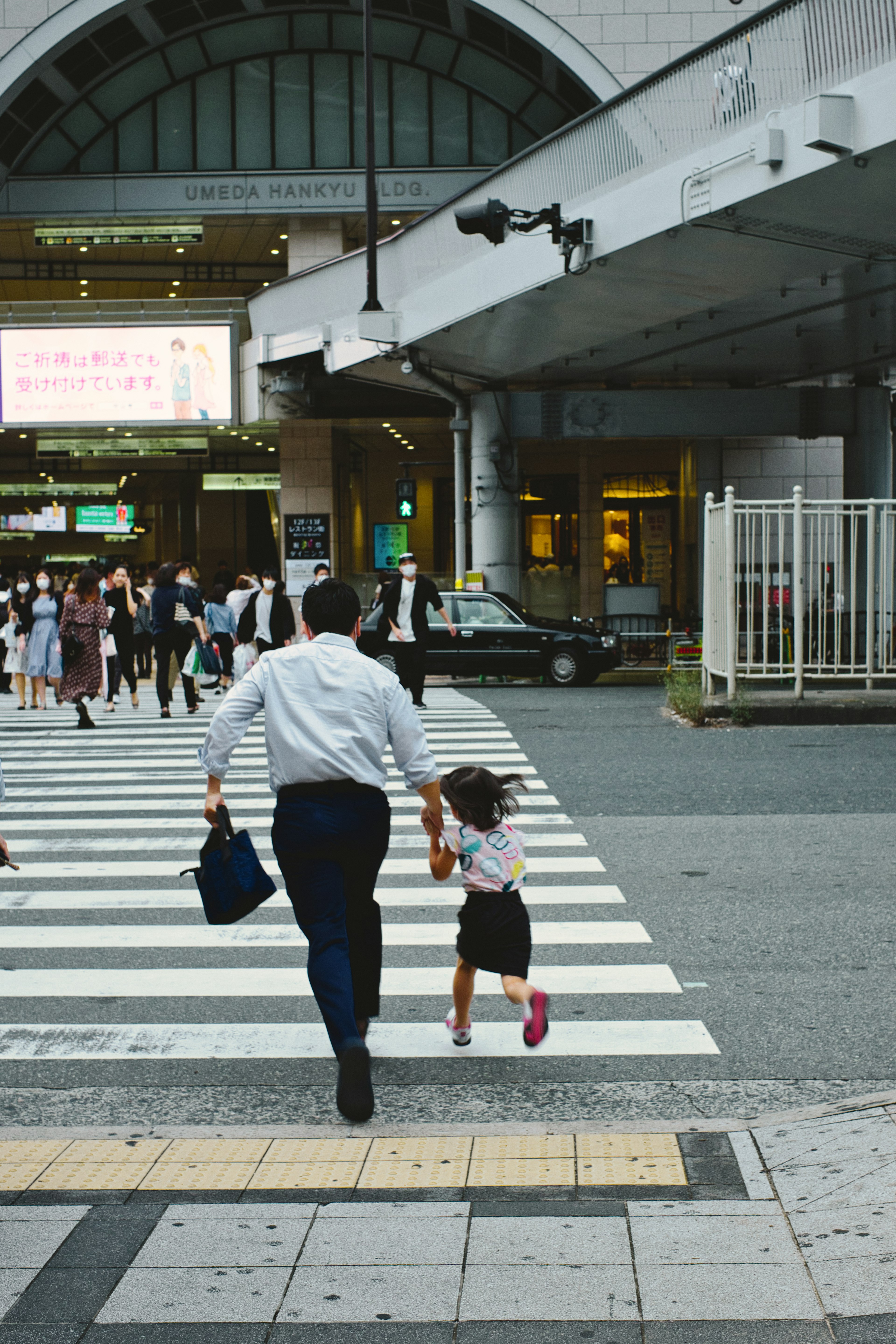 Father and young girl crossing the street surrounded by pedestrians