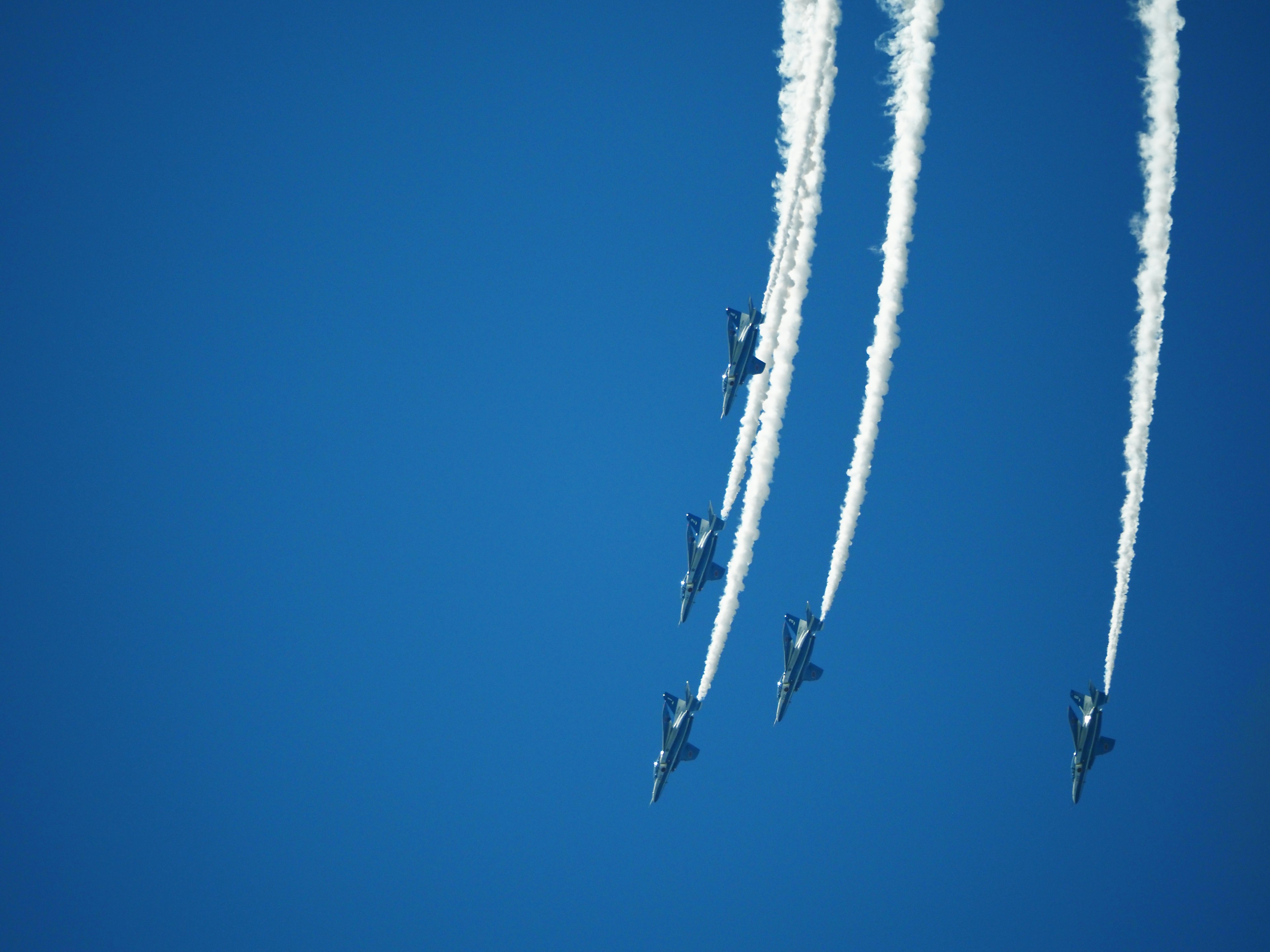 Formation de plusieurs chasseurs volant contre un ciel bleu avec des traînées de fumée blanche