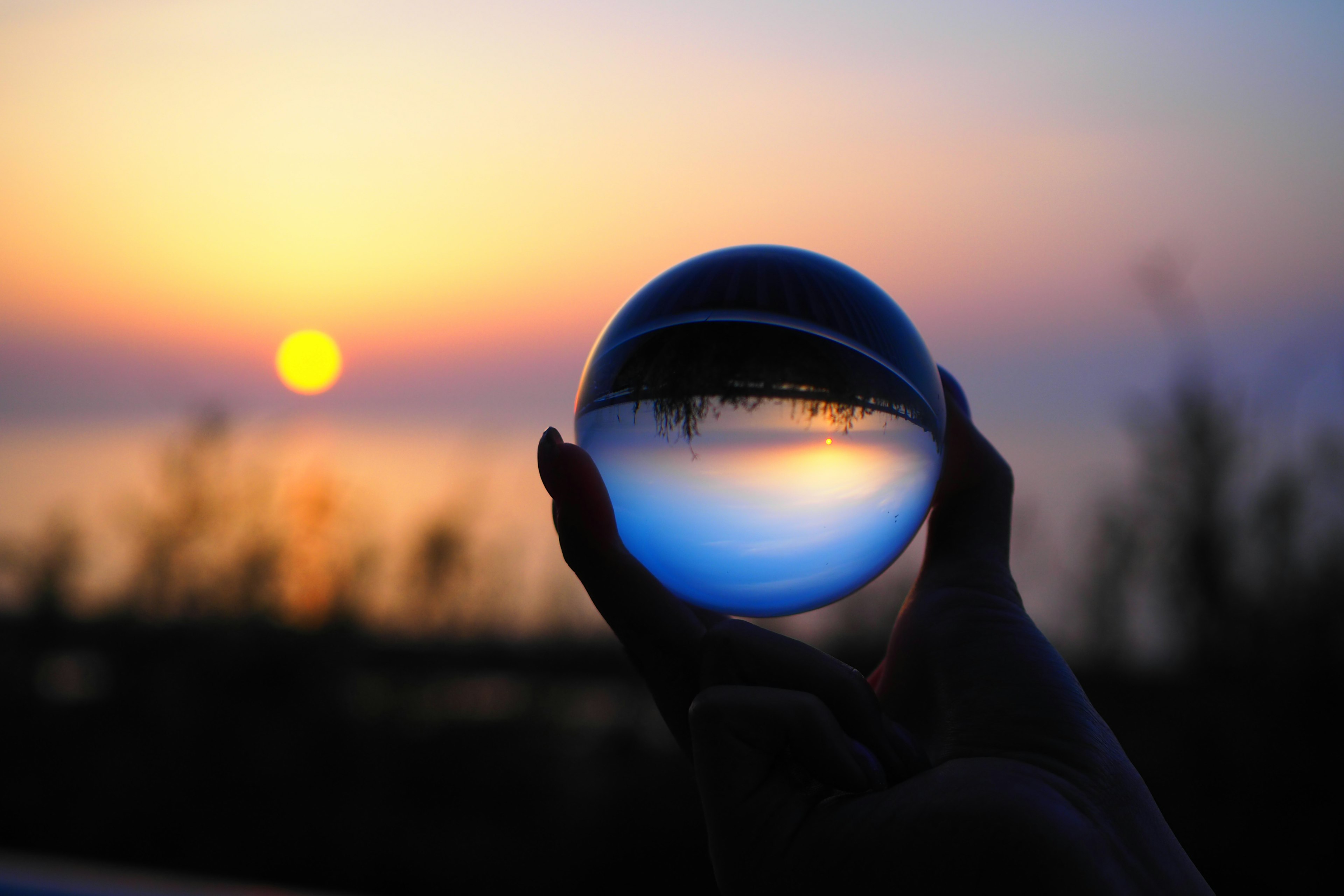 Silhouette einer Hand, die eine Kristallkugel hält, die einen Sonnenuntergang reflektiert