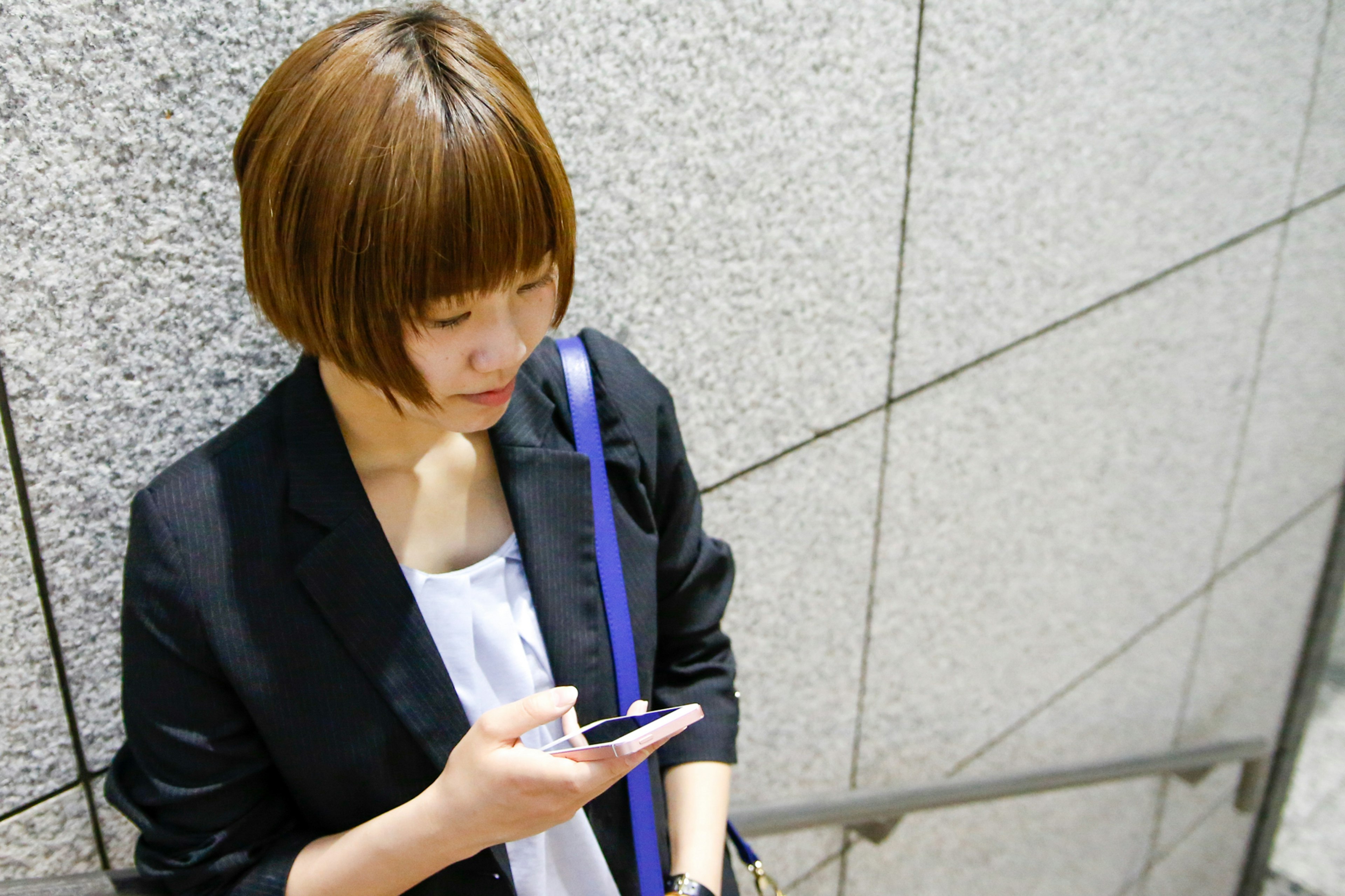 A woman with short hair using a smartphone while leaning against a wall