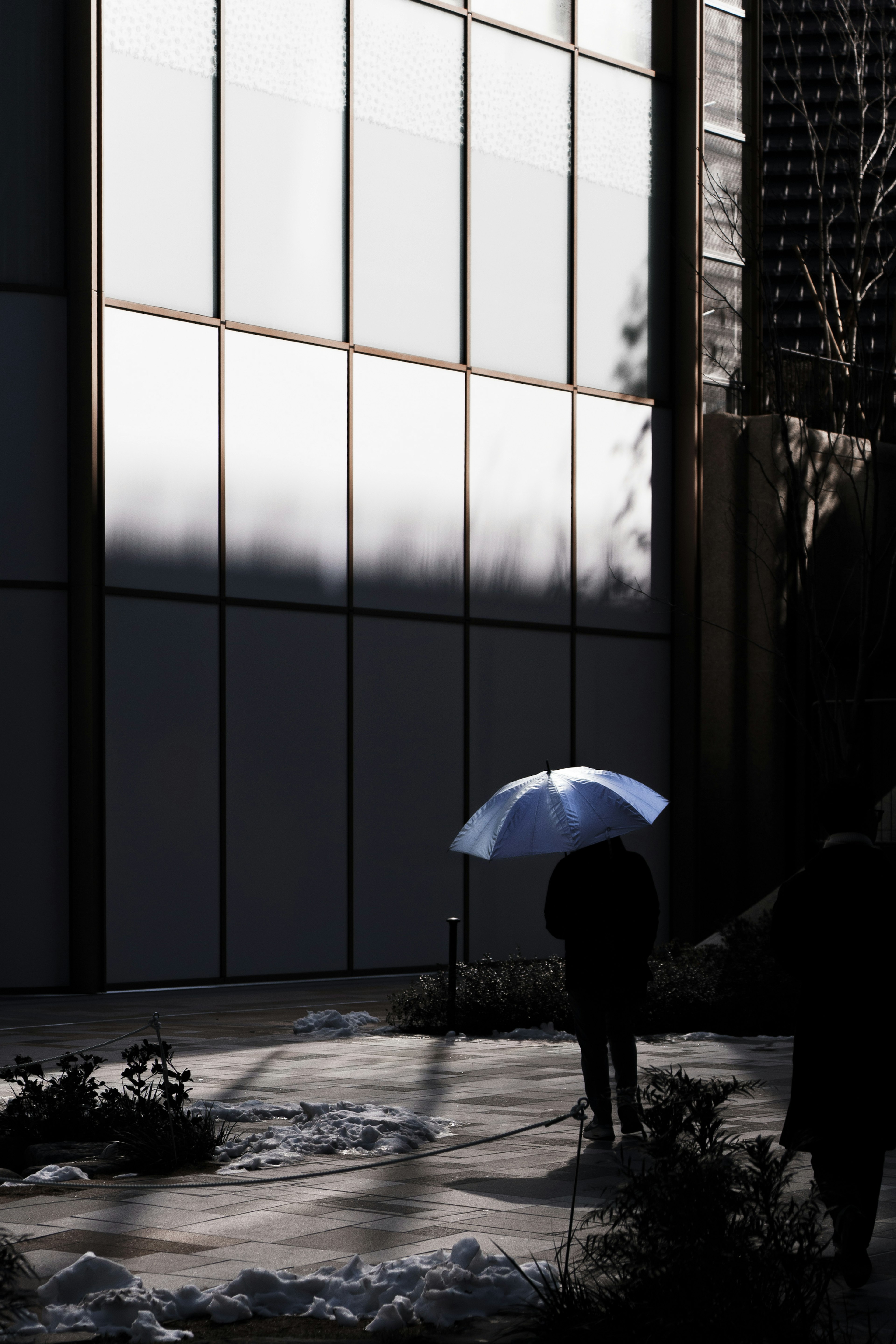 Silhouette di una persona che cammina con un ombrello accanto a un edificio moderno