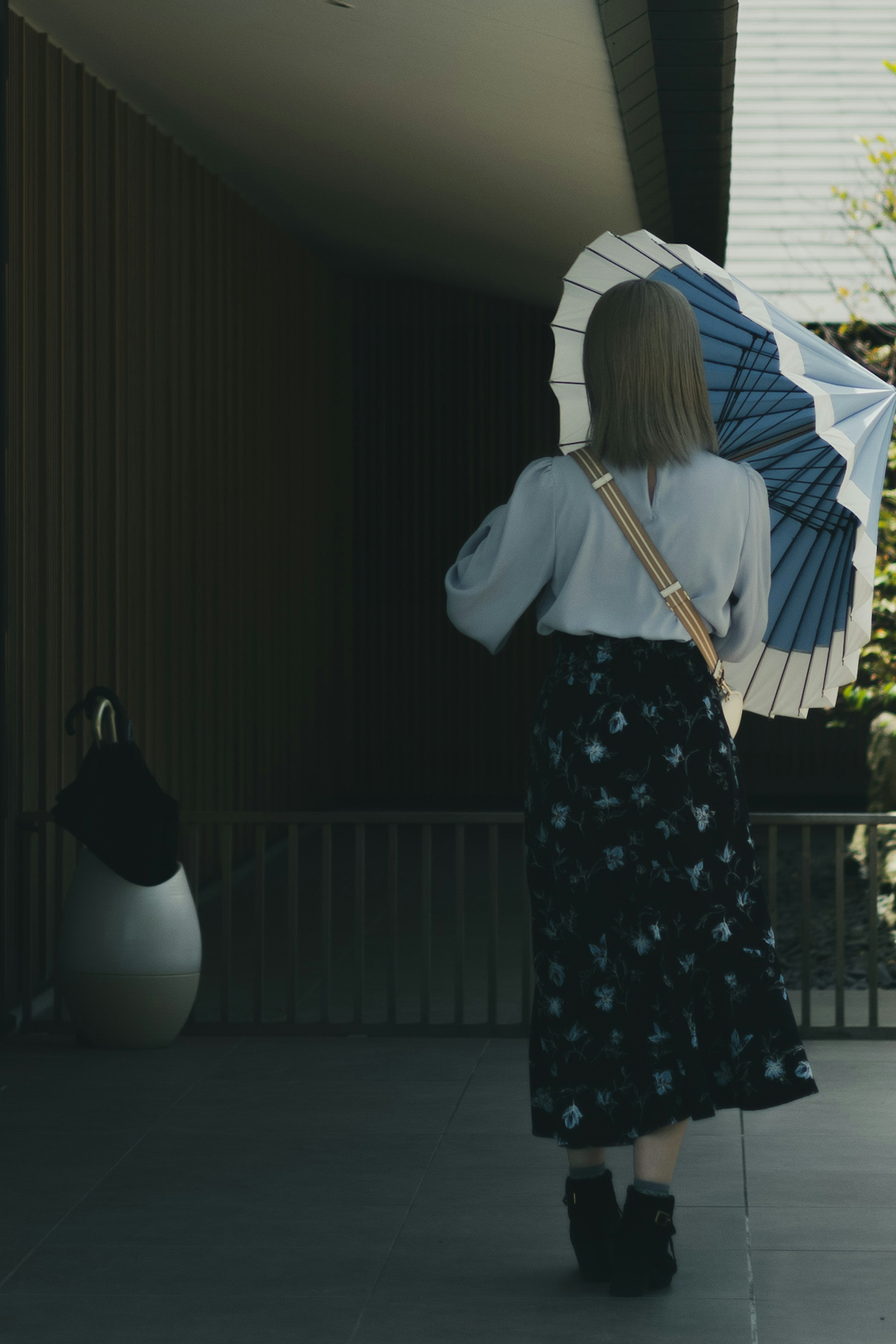 Una donna che cammina verso l'ingresso di un edificio con un ombrello blu