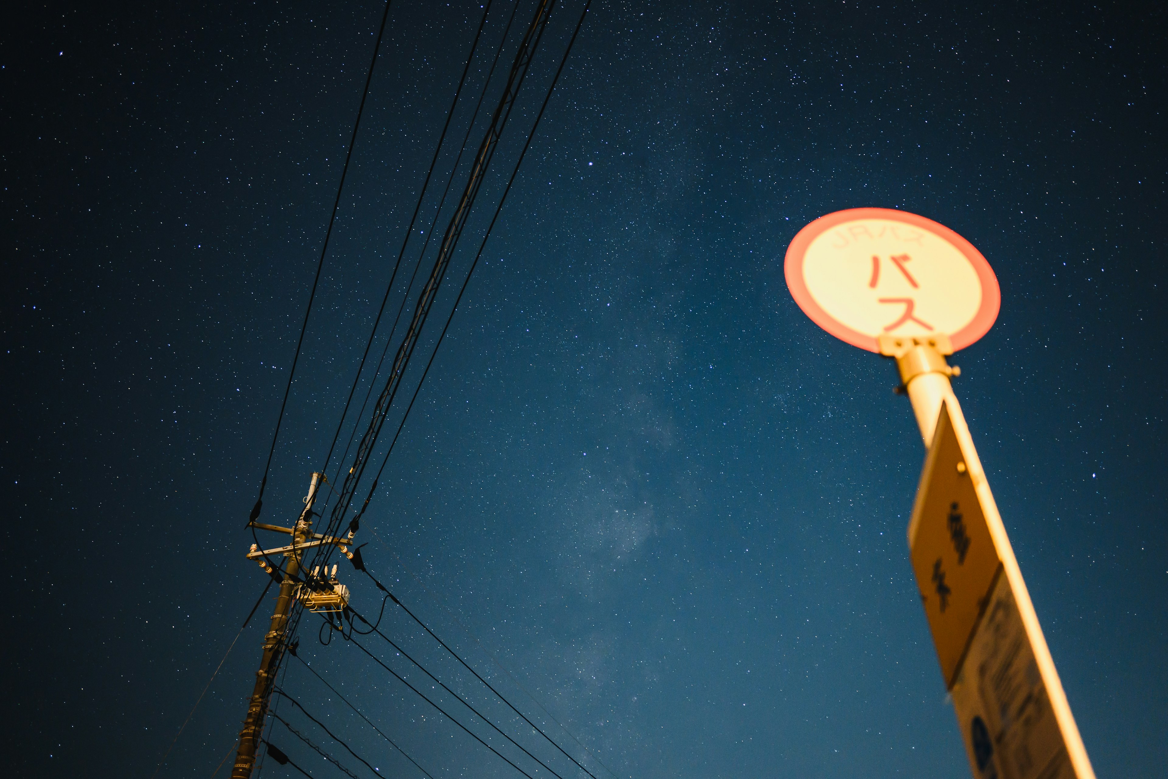 Bus stop sign under a starry sky with power lines