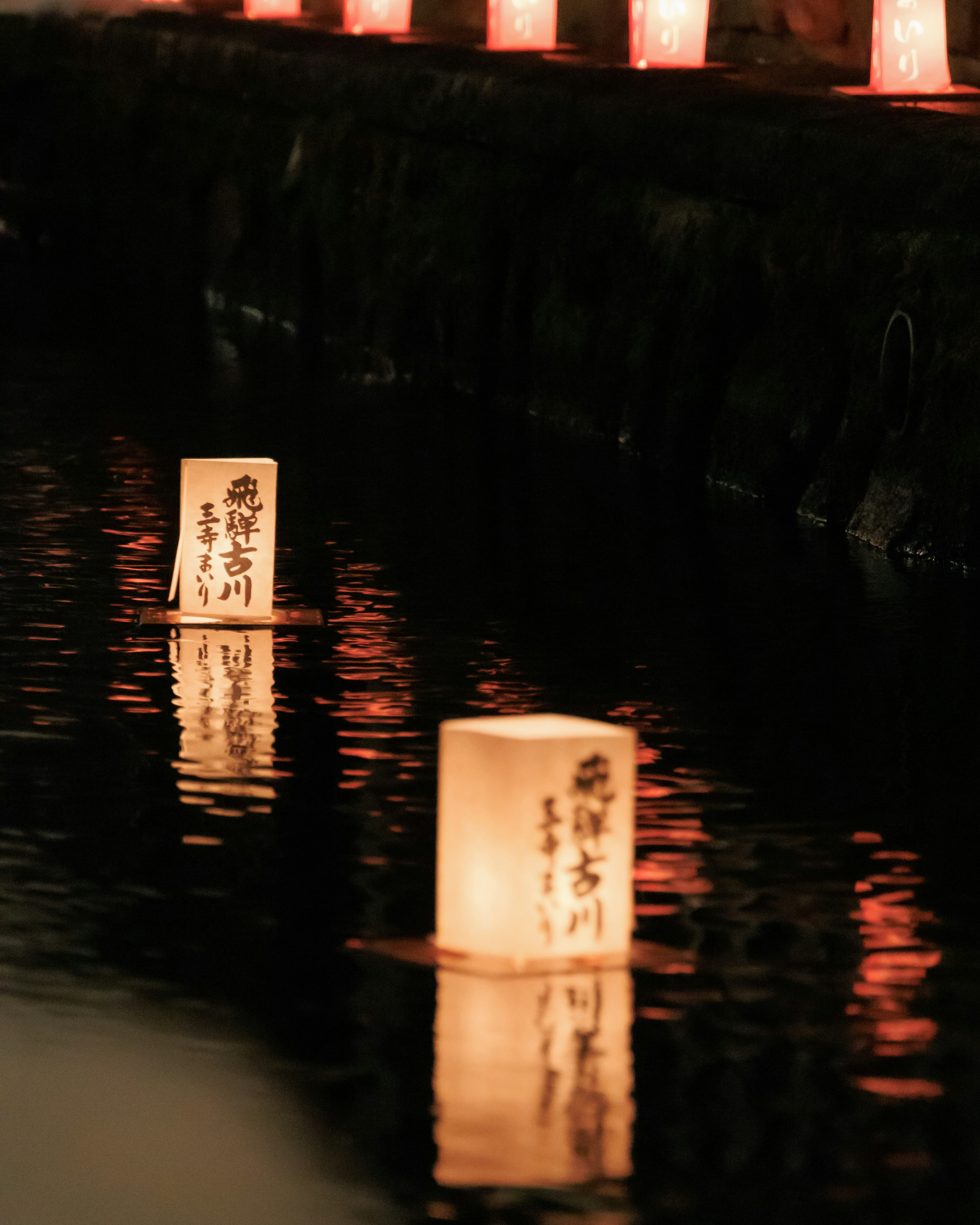 Scène nocturne magnifique avec des lanternes flottant sur l'eau et leurs reflets