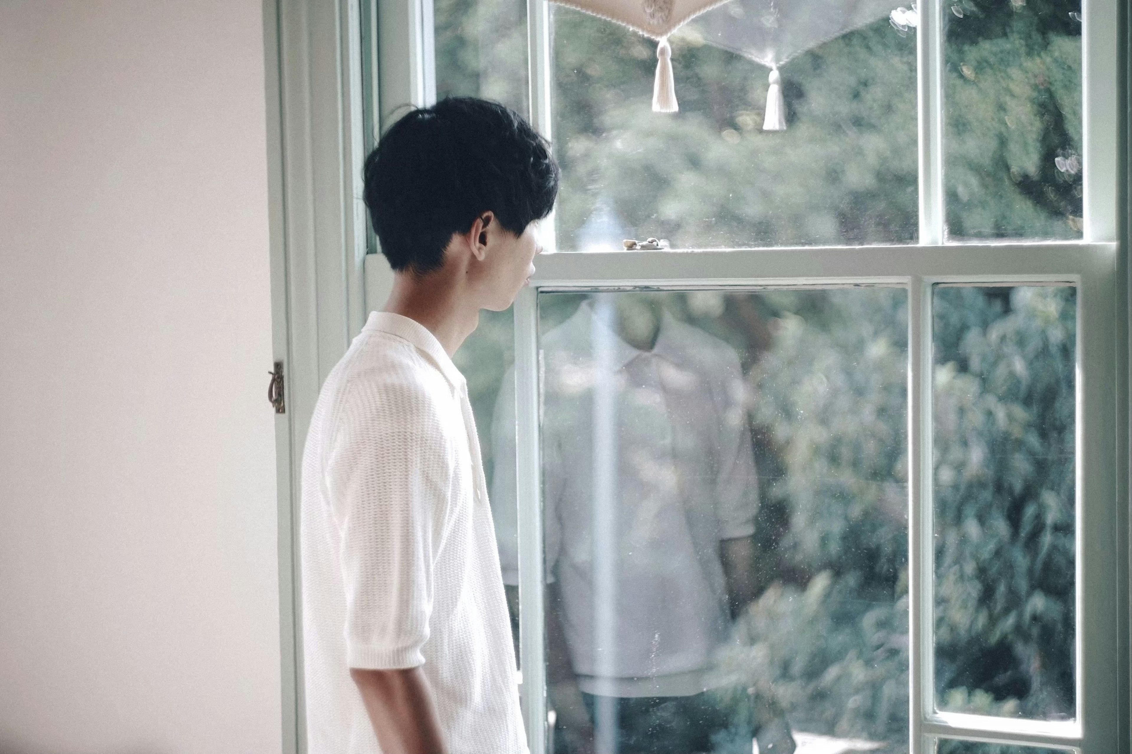 Perfil de un hombre mirando por la ventana con una camisa blanca luz natural entrando en la habitación