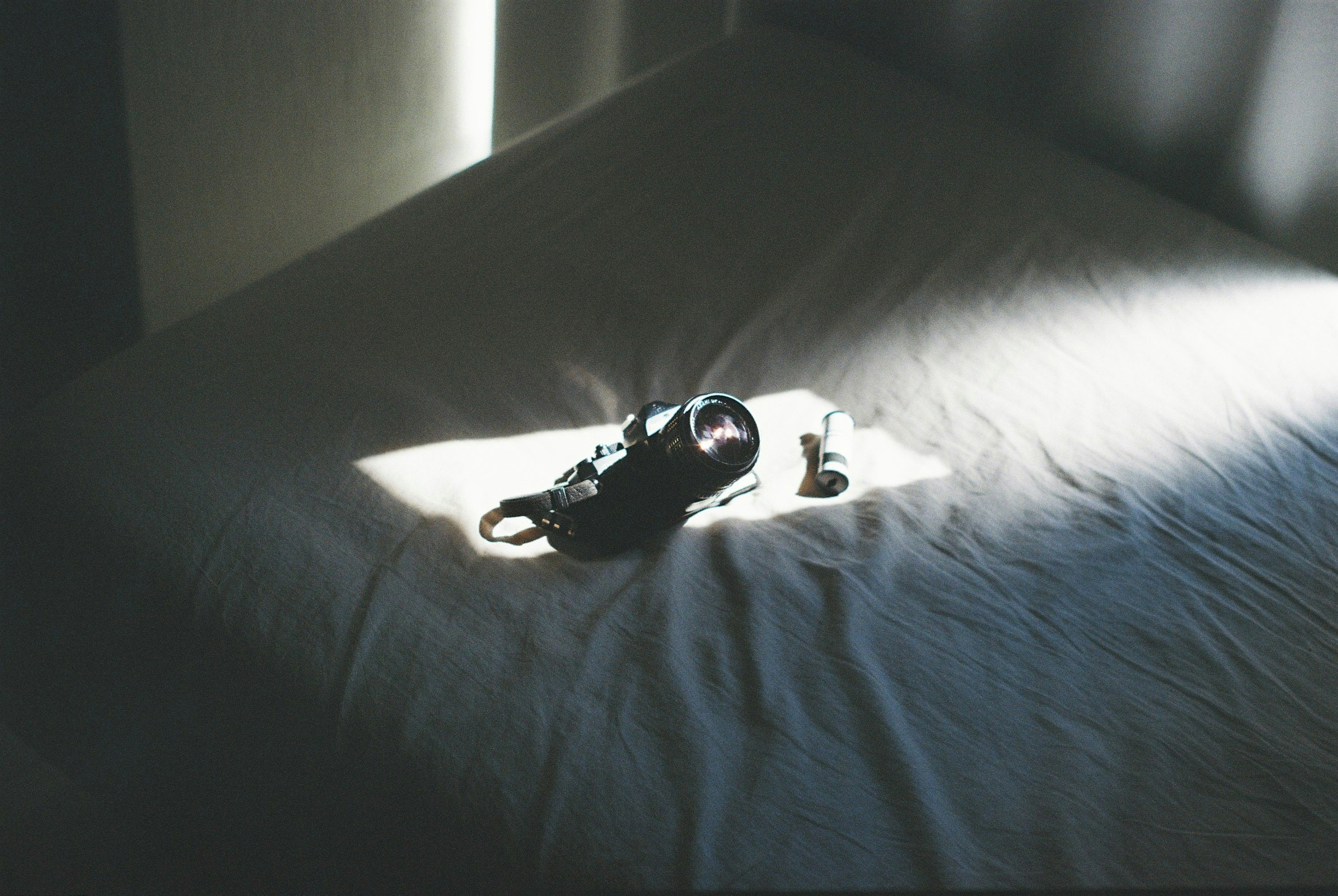 Camera and small items placed on a bed with bright light shining through