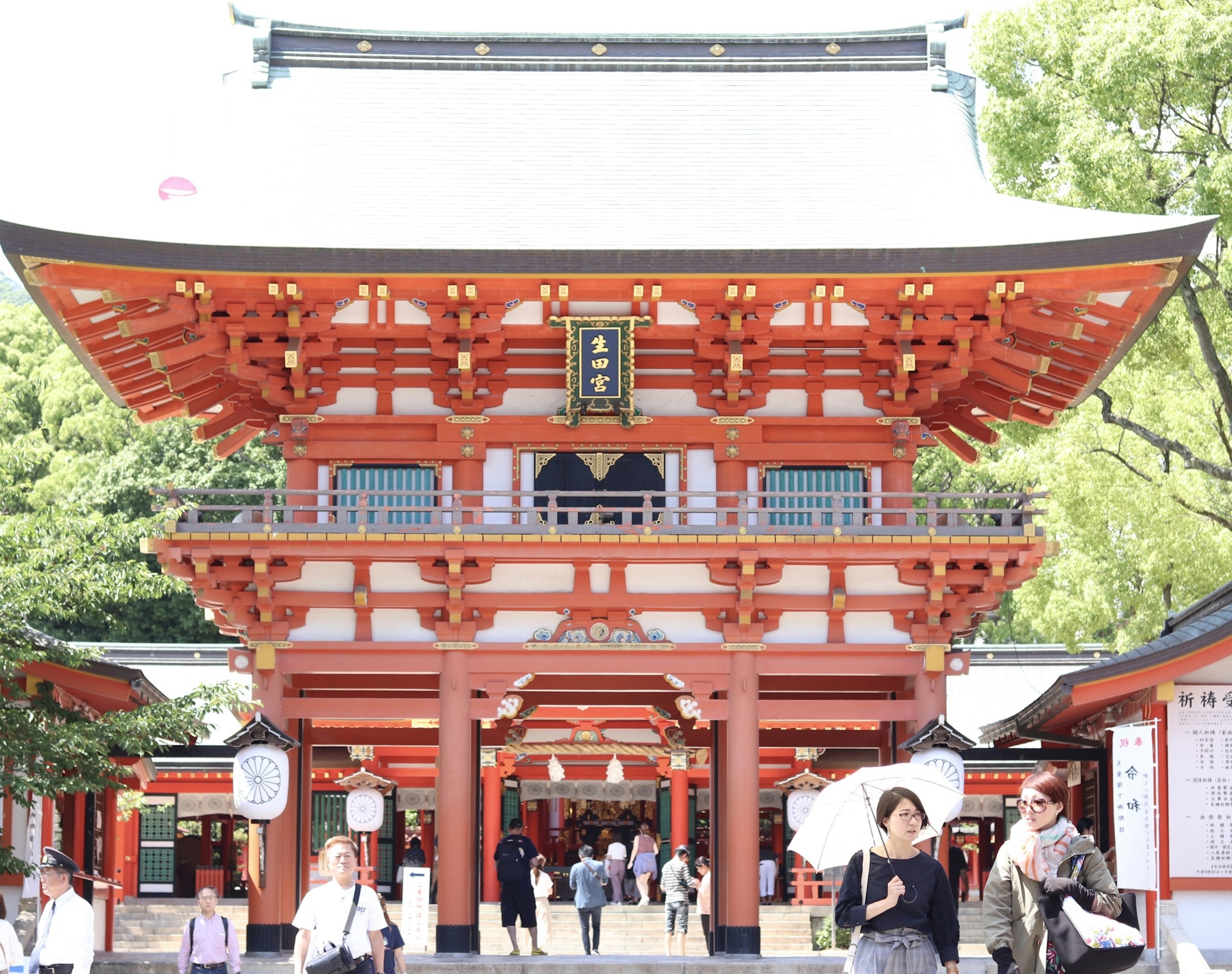 View of a traditional red shrine with visitors and green surroundings