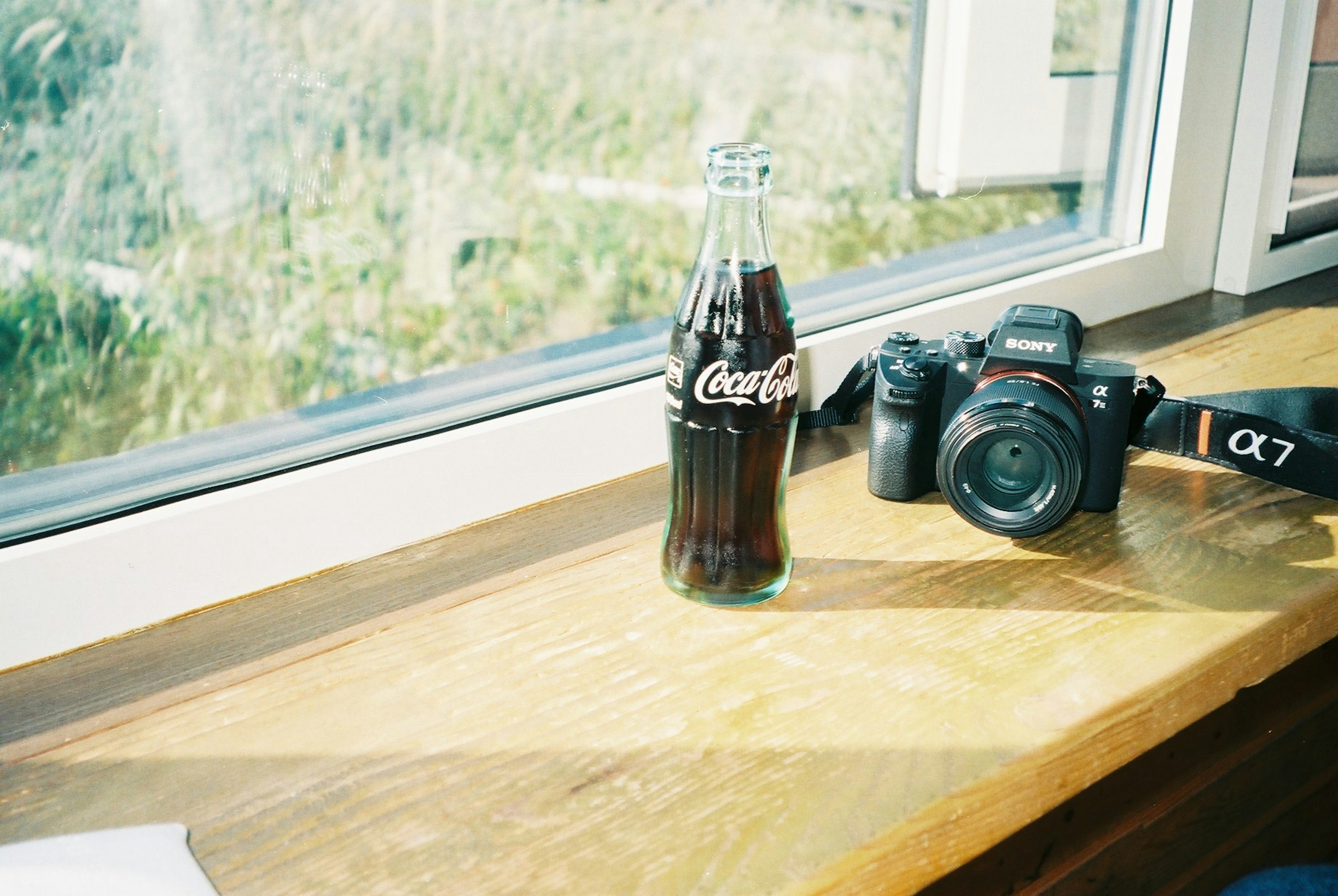 Botol Coca-Cola dan kamera di atas meja kayu di dekat jendela