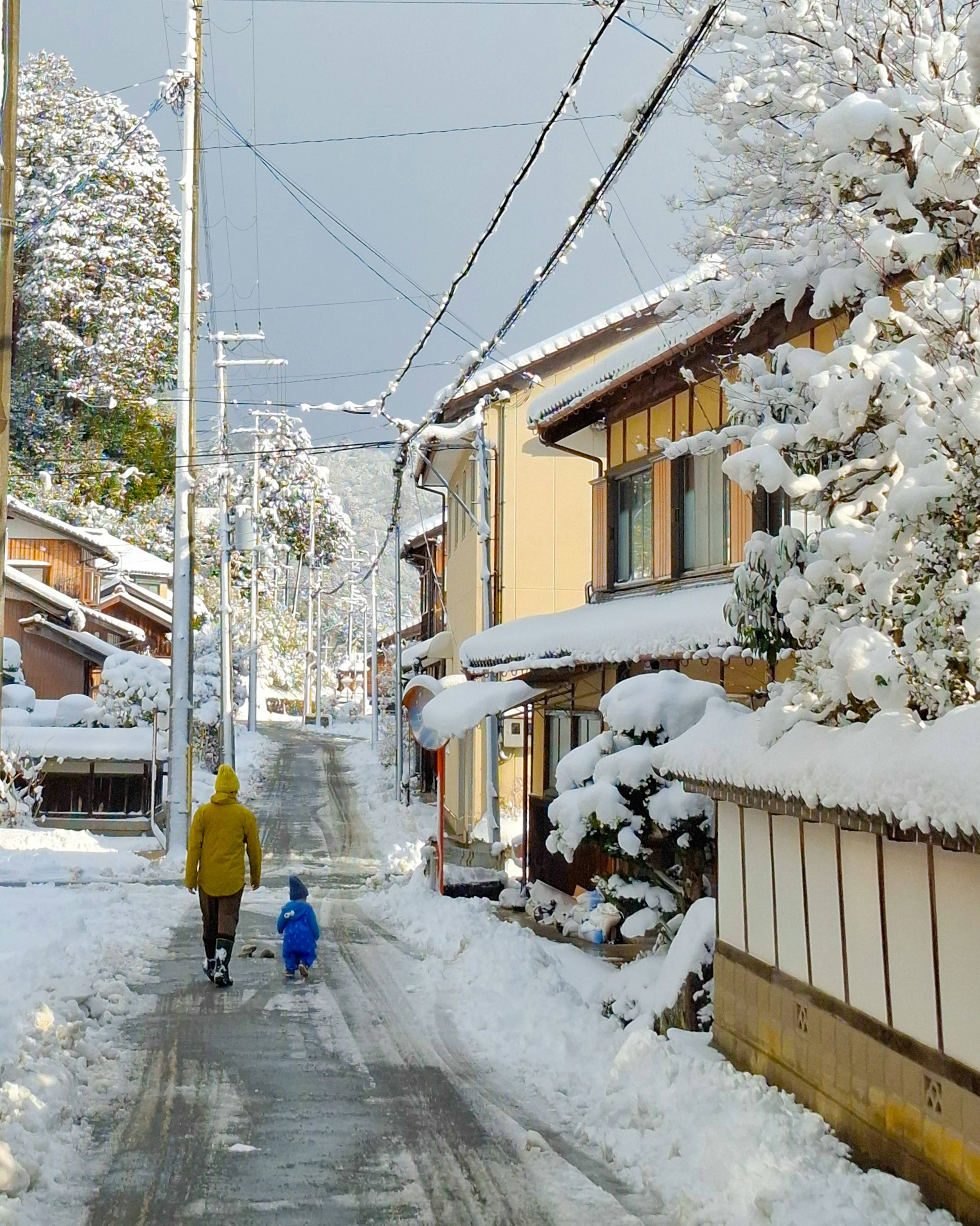 Parent and child walking down a snow-covered street in a Japanese village