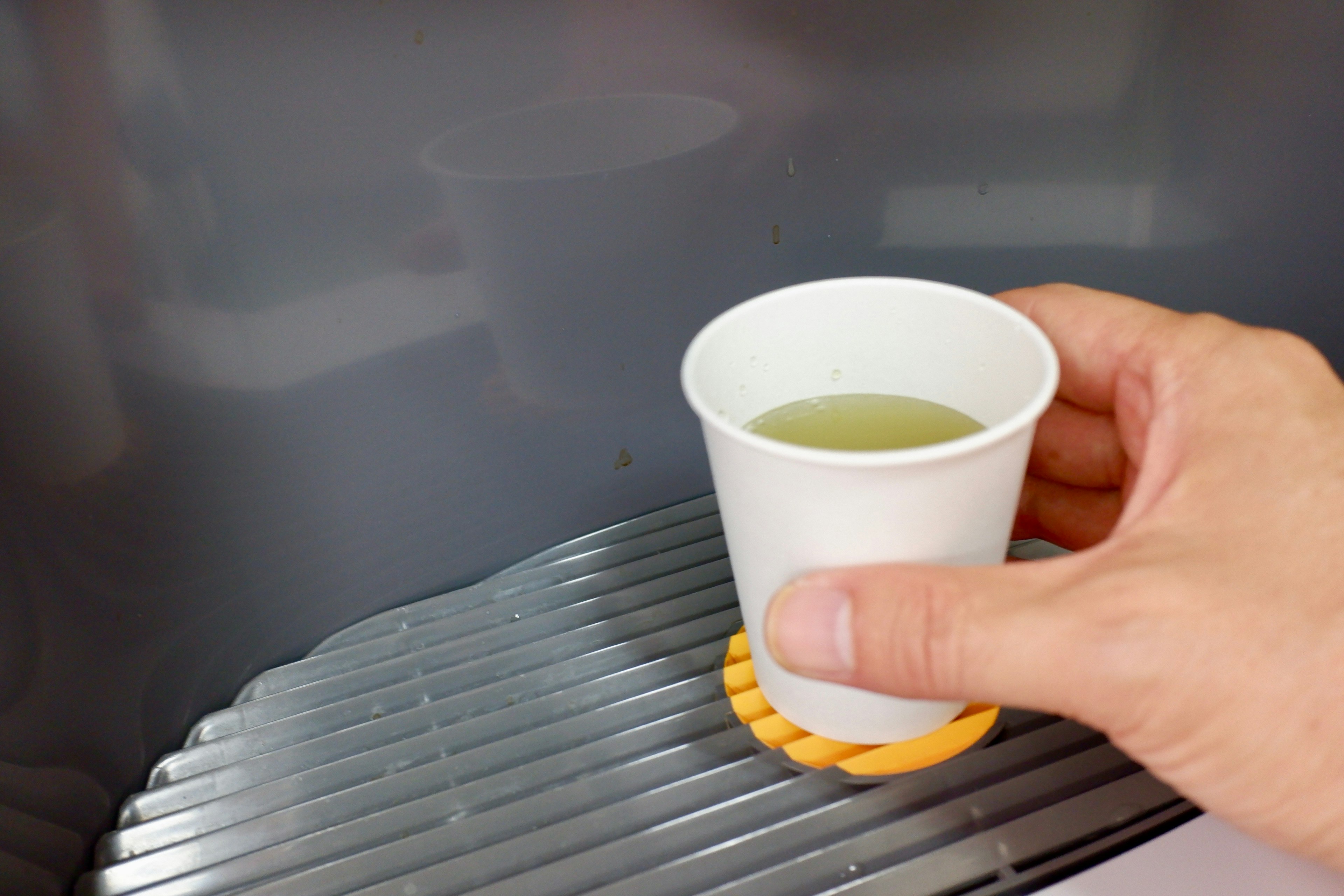 A hand holding a white paper cup with a drink being poured