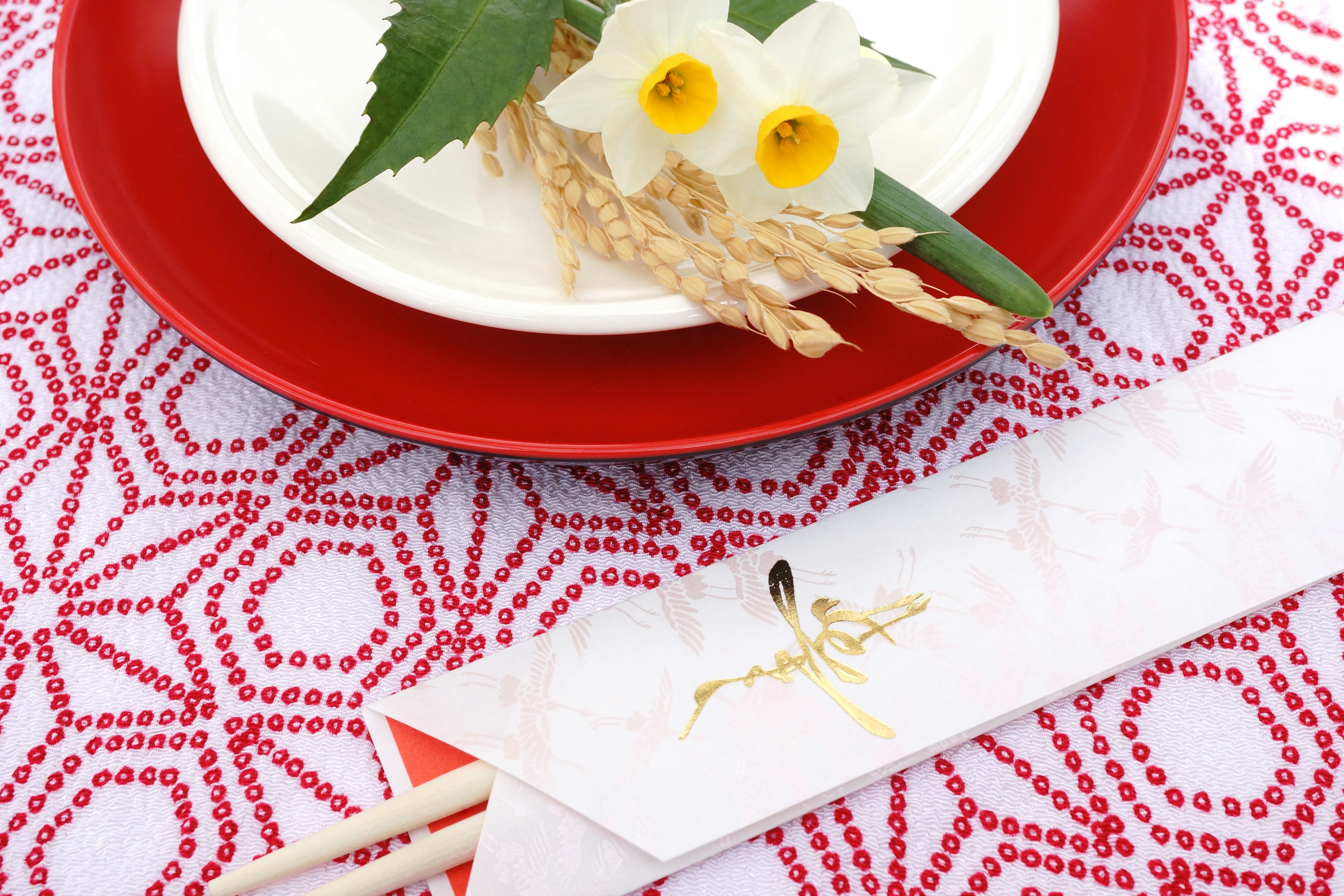 Impostazione della tavola in stile giapponese con un piatto rosso un piatto bianco e fiori con foglie di bambù