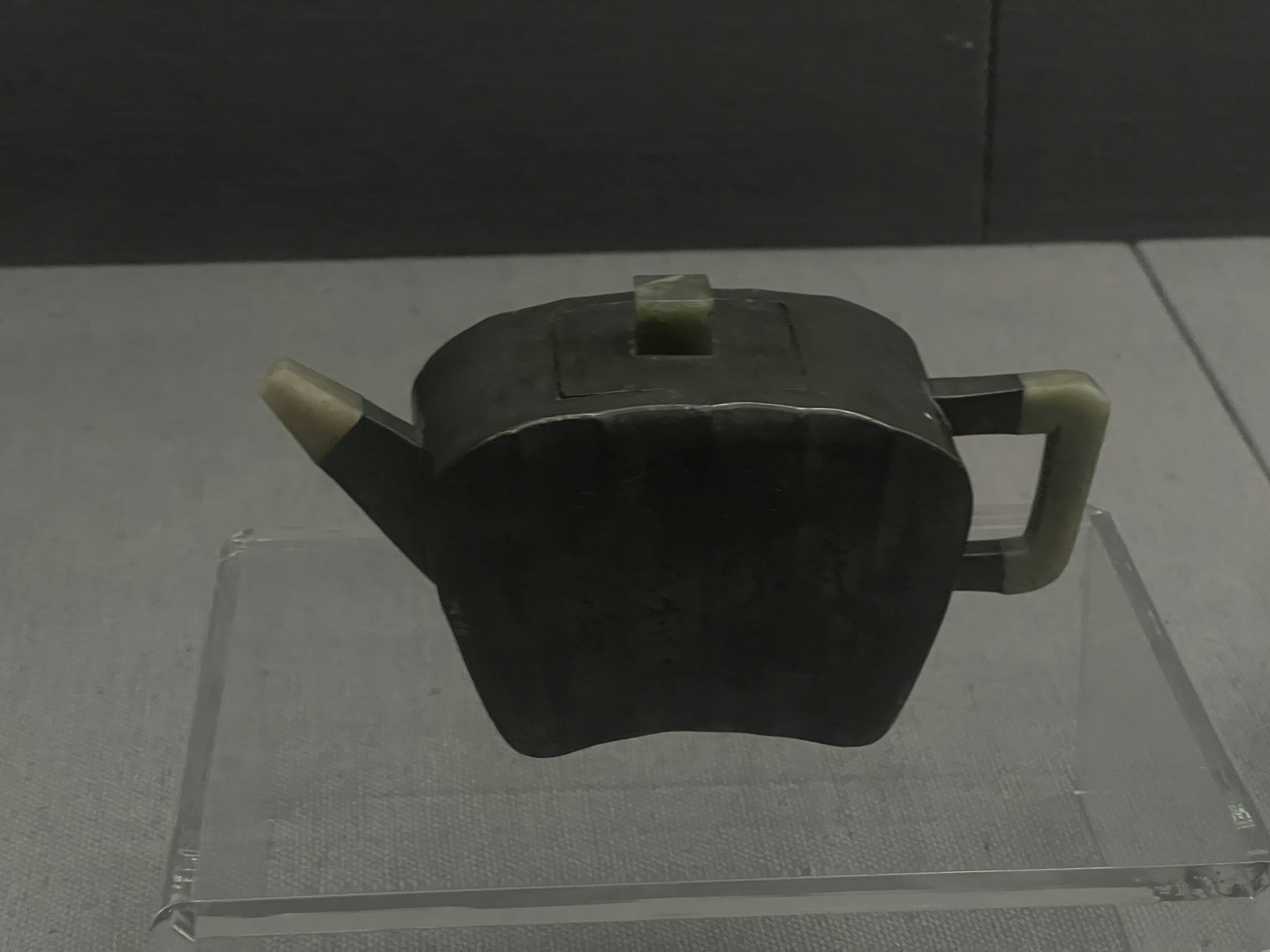 The image shows a square-shaped teapot made of black stone displayed on a stand