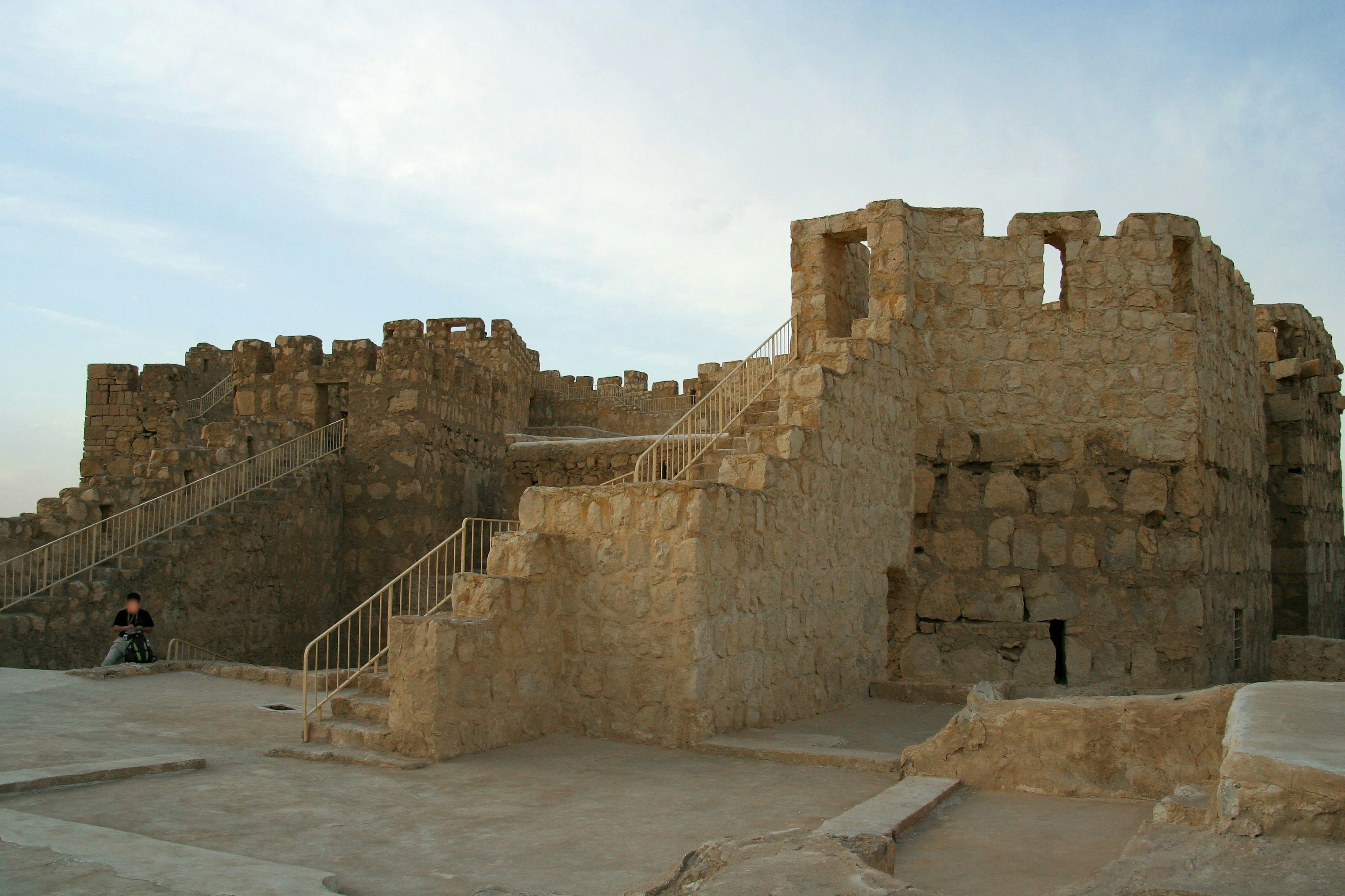 Ruines d'un château ancien avec des escaliers et des murs sous un ciel de coucher de soleil