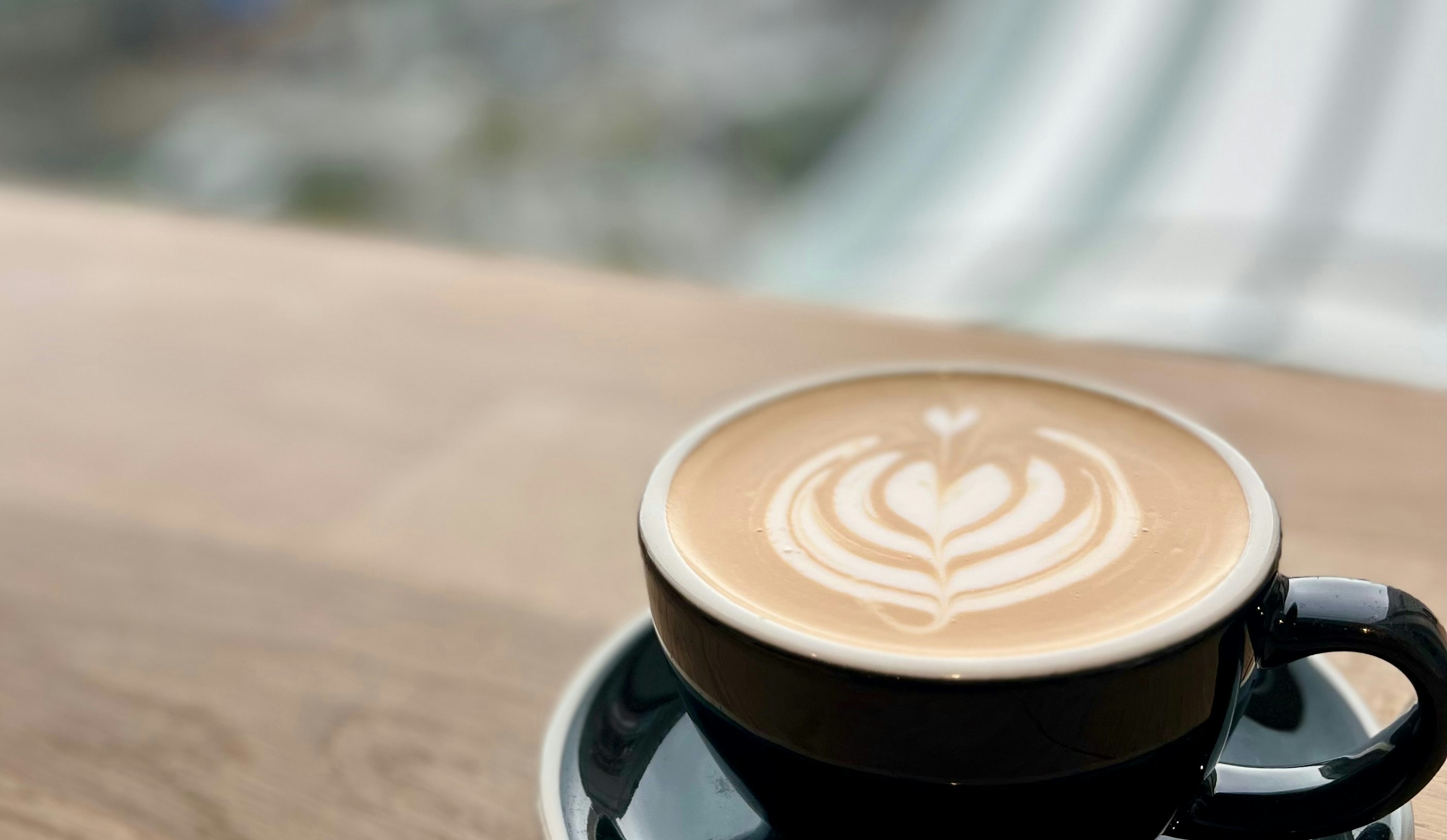 Kopi dengan seni latte dalam cangkir hitam di atas meja kayu