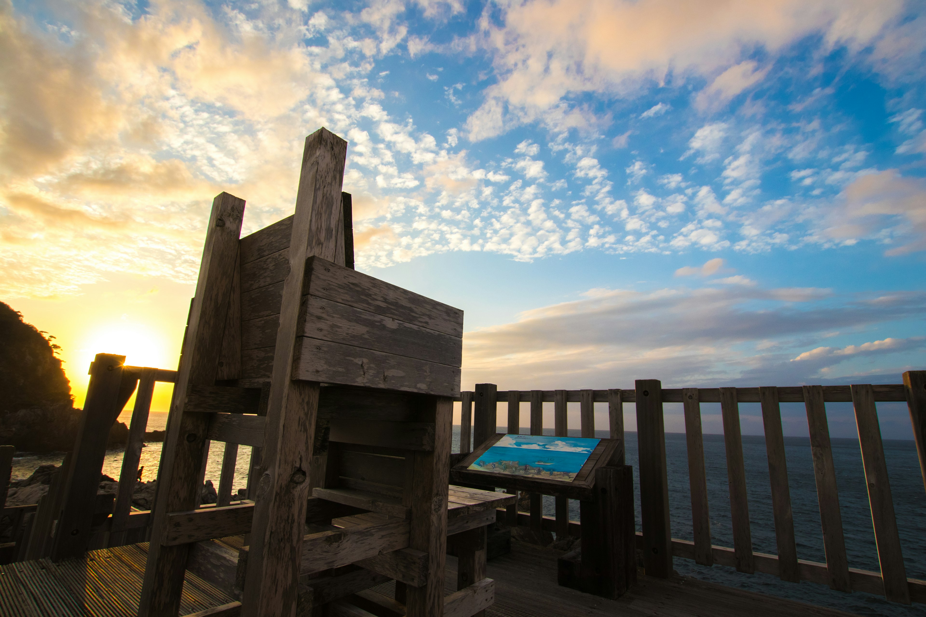 Chaise en bois surplombant la mer avec coucher de soleil et nuages colorés