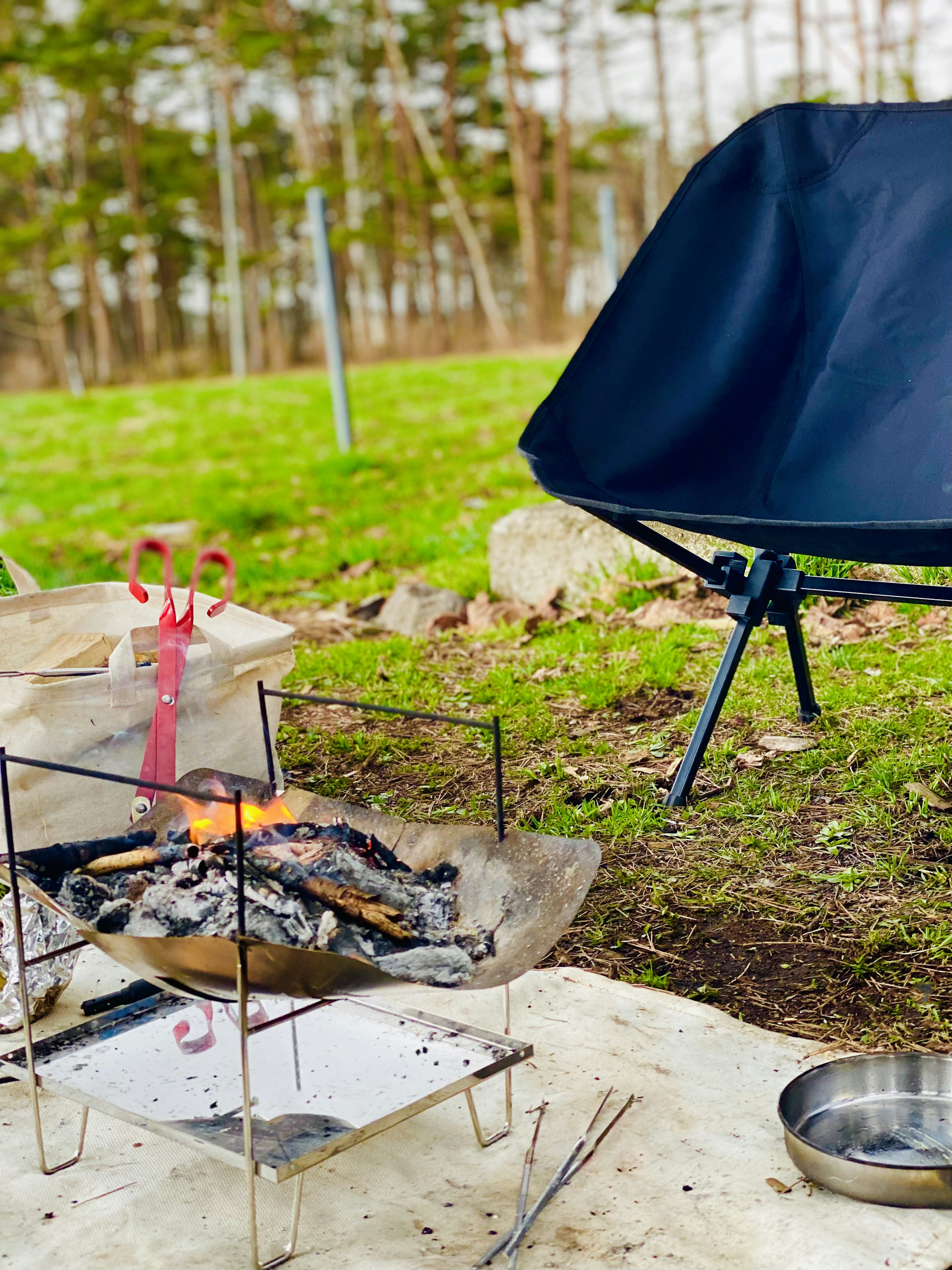 Escena al aire libre con una silla compacta y una parrilla frente a una fogata