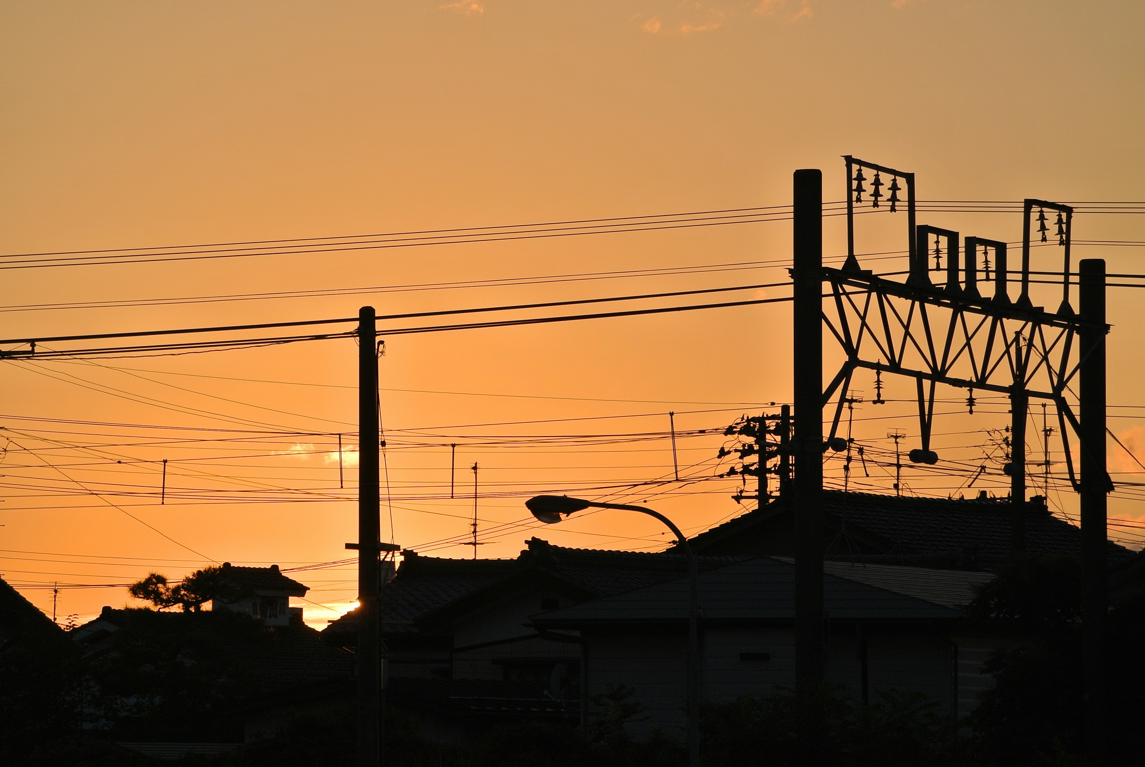 Silhouette of power lines and houses against a sunset