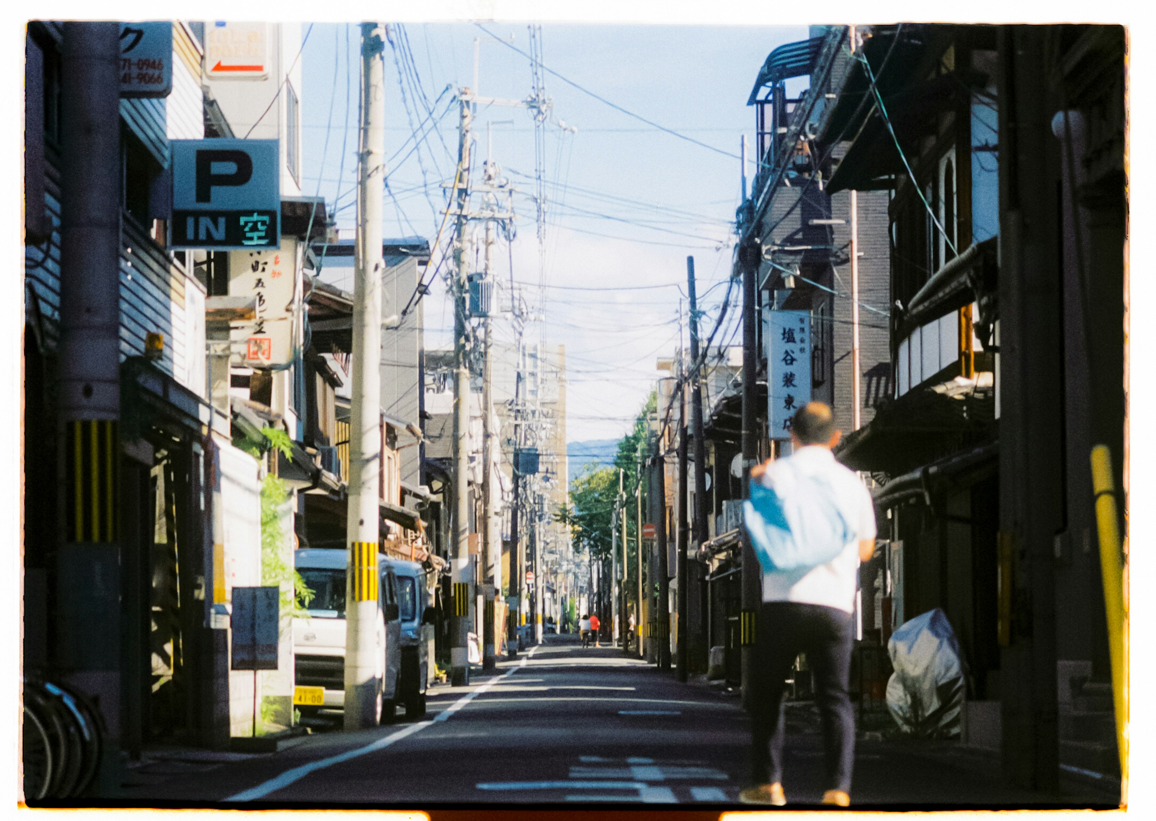 A person walking down a quiet street with old buildings and power lines