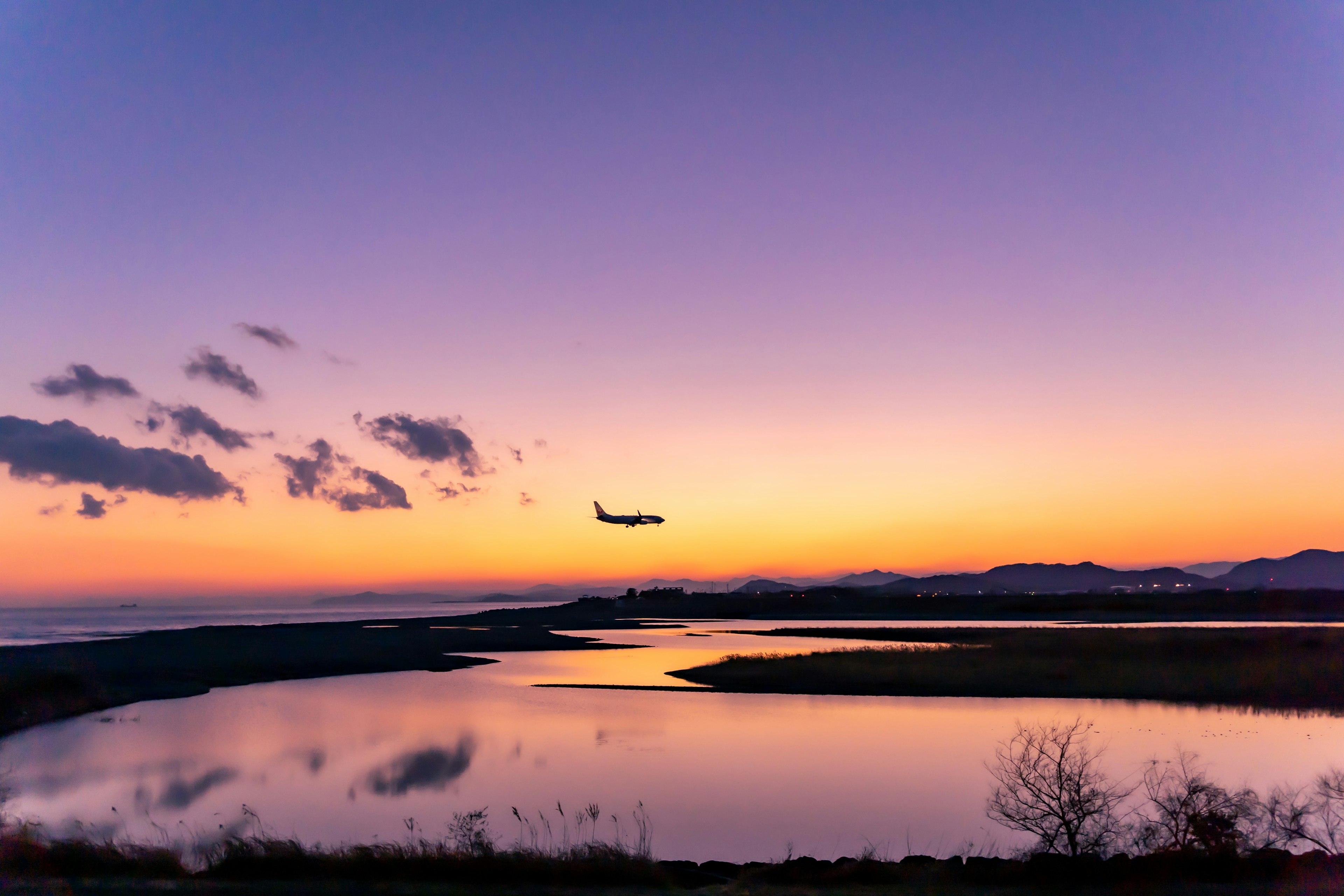 Un avión aterrizando contra un cielo de atardecer reflejándose en el agua