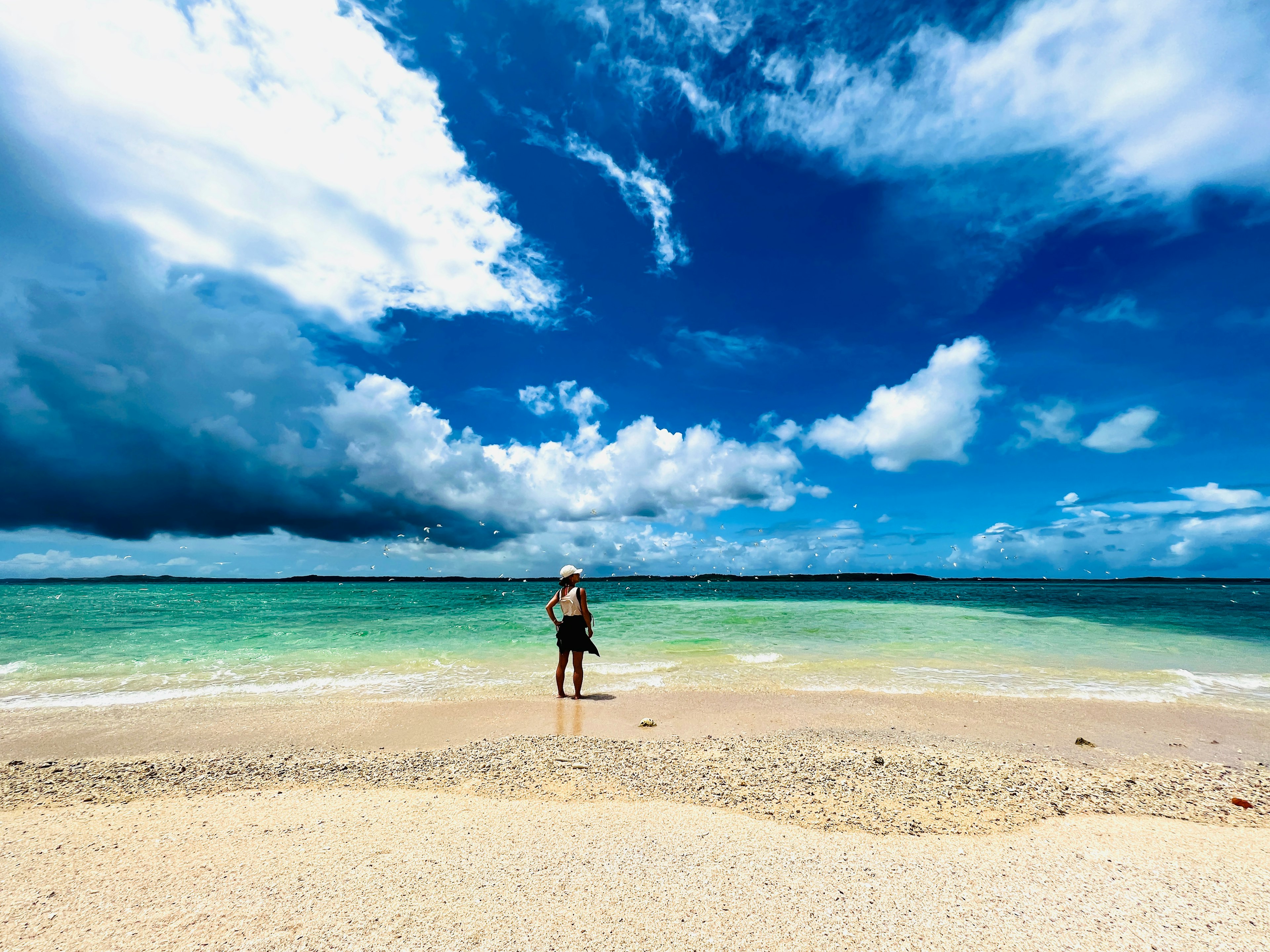 Una persona in piedi su una spiaggia di sabbia con una vista bellissima del cielo e del mare blu