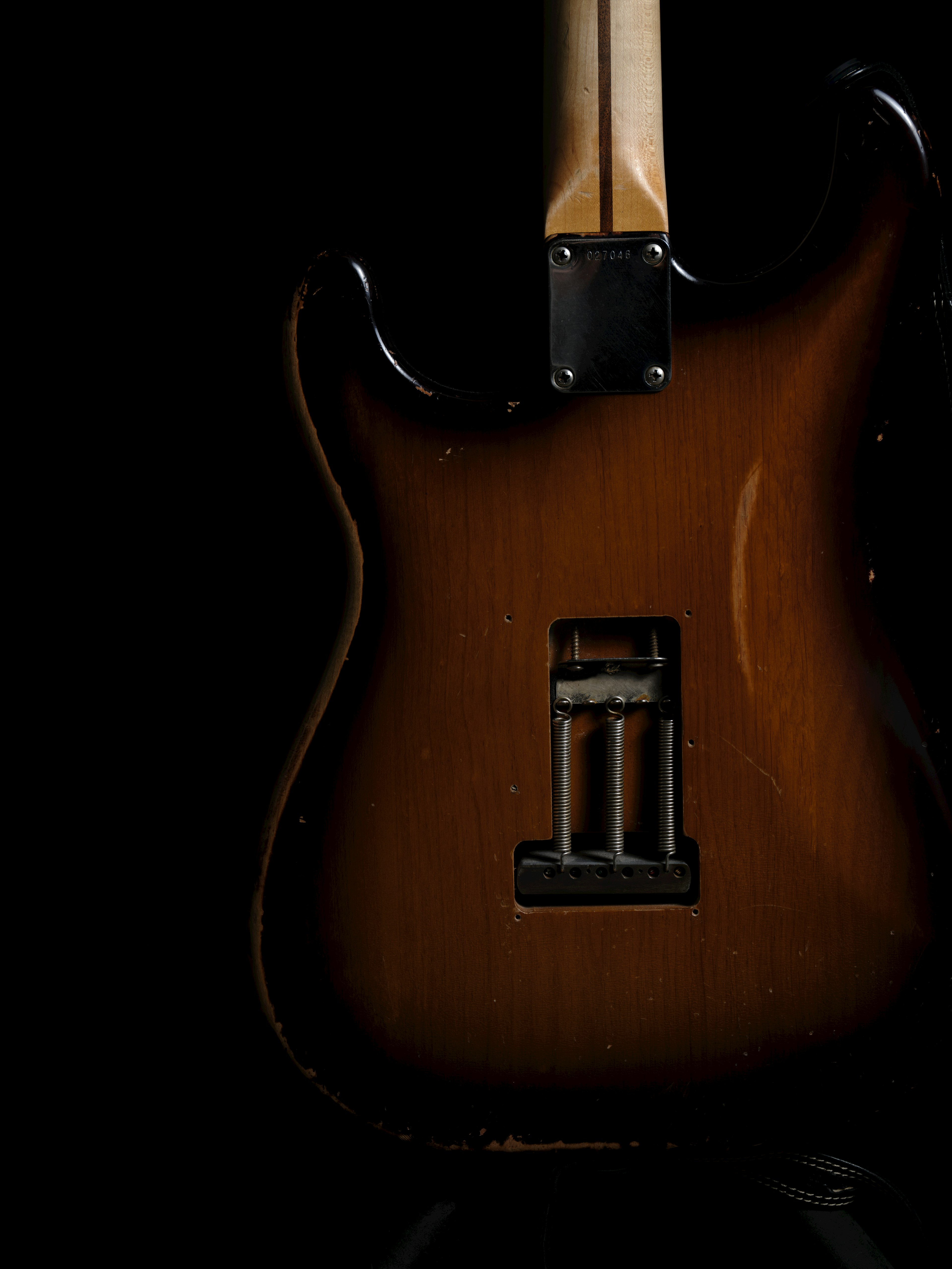 Back view of a brown electric guitar against a black background