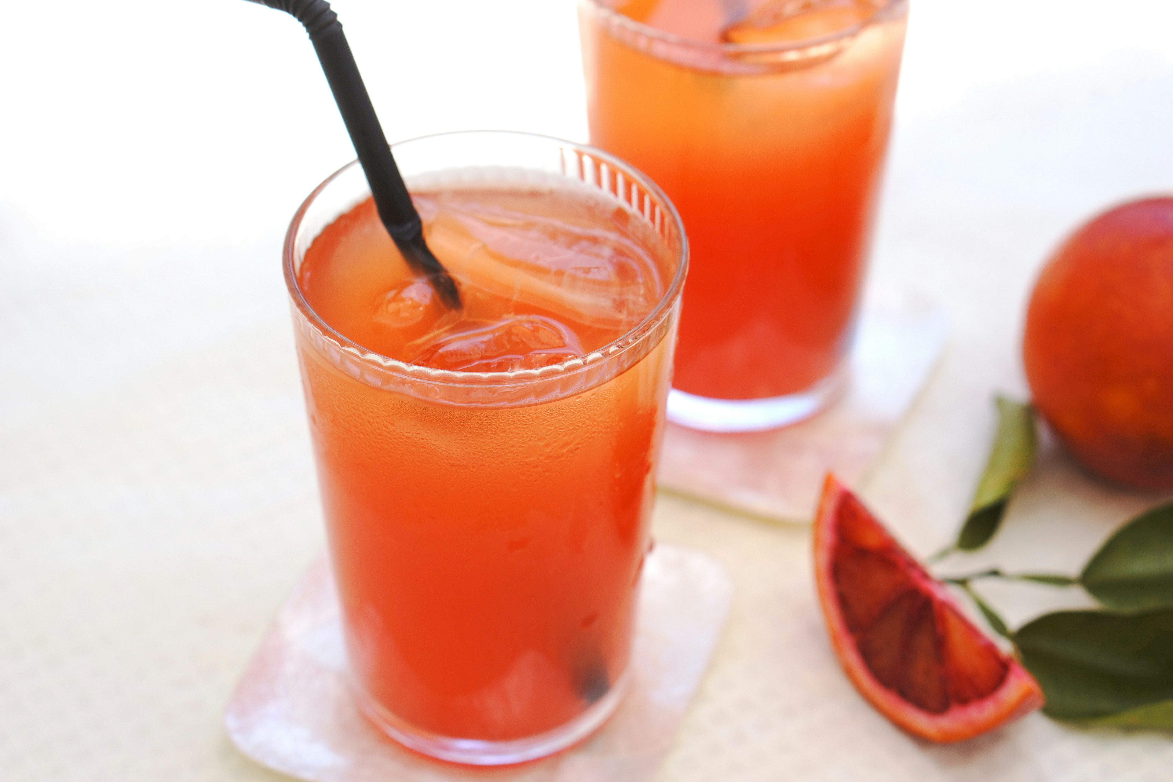 Dos vasos de jugo de naranja sanguina con hielo y una pajilla