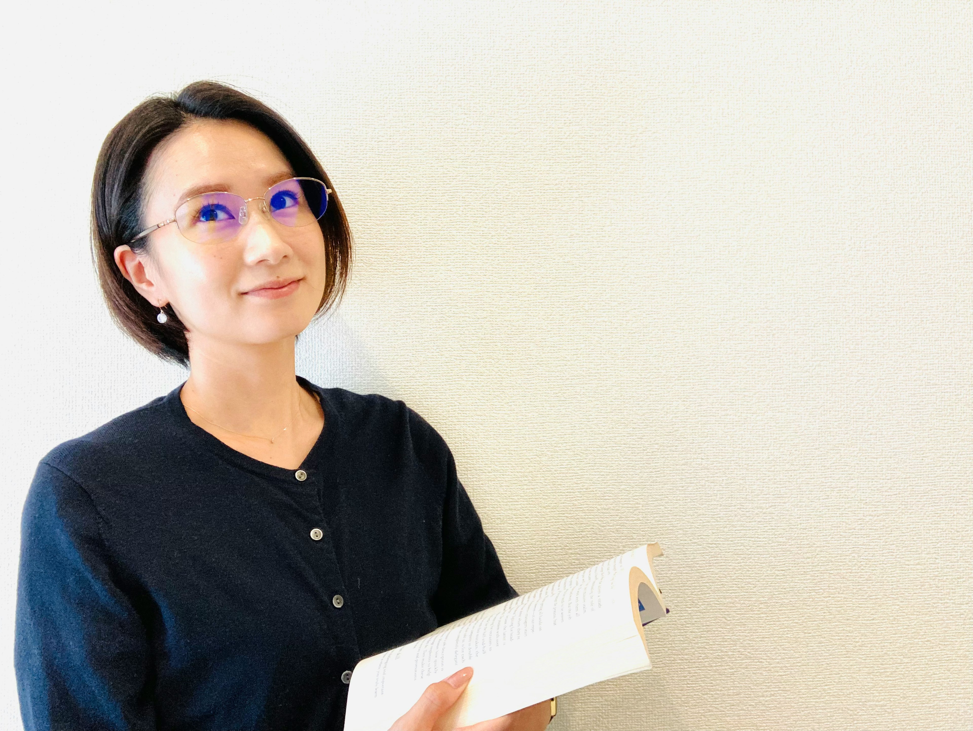 Woman smiling while holding a book in front of a white wall