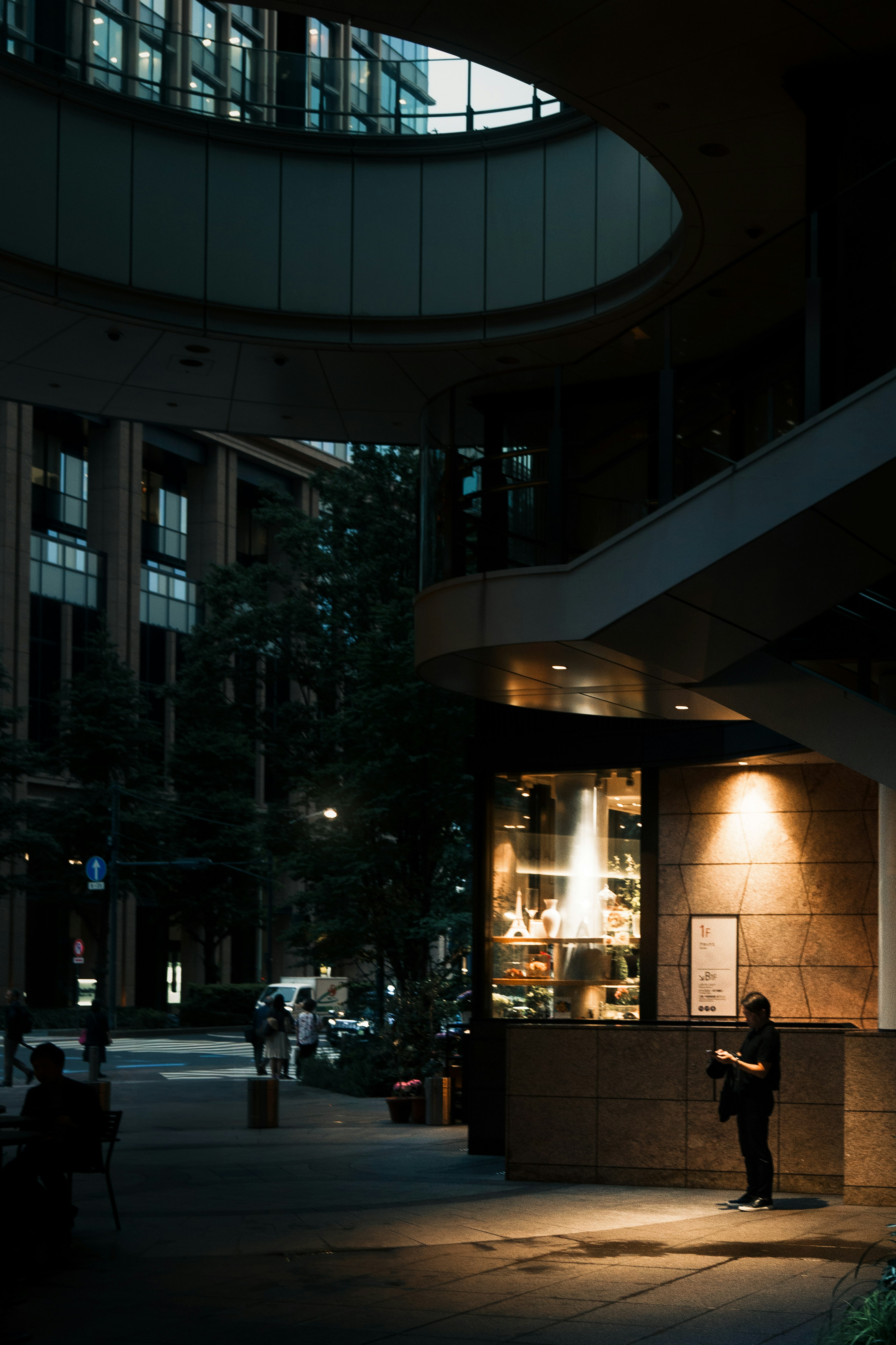 Person standing in a dimly lit street corner with bright store lighting