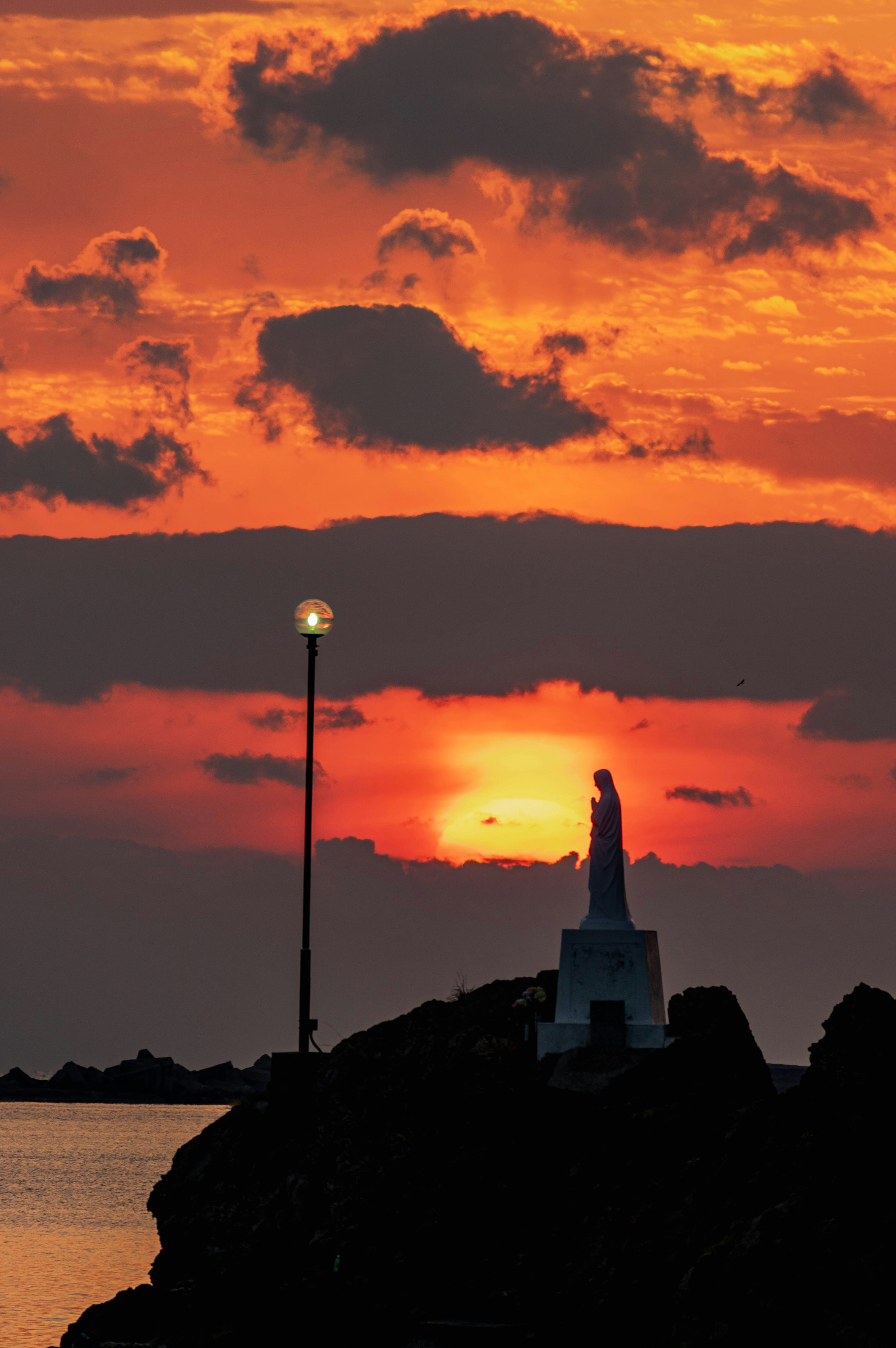 Silhouette einer Statue und einer Laterne vor einem Sonnenuntergang