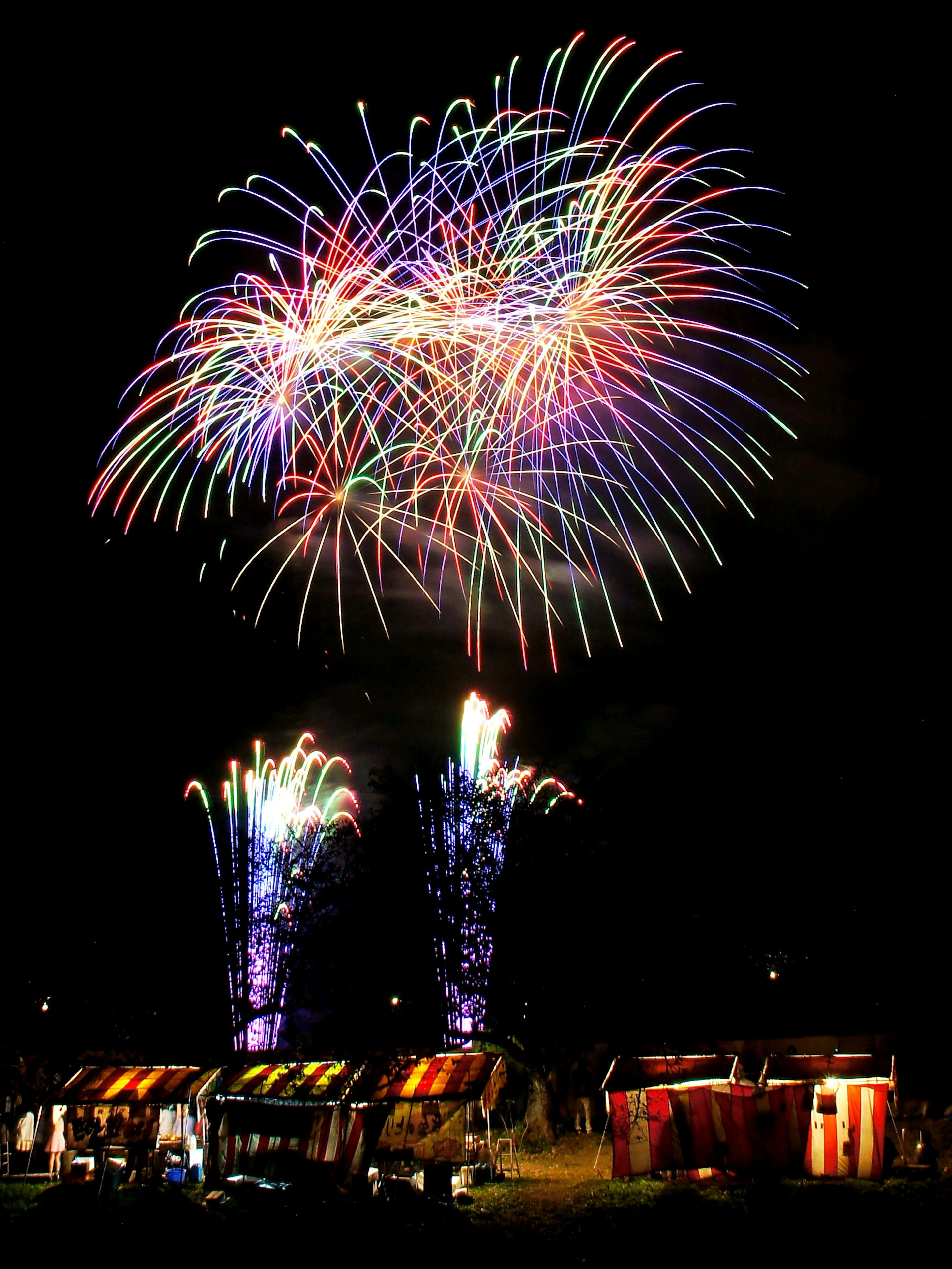 Fuegos artificiales coloridos estallan en el cielo nocturno con puestos abajo