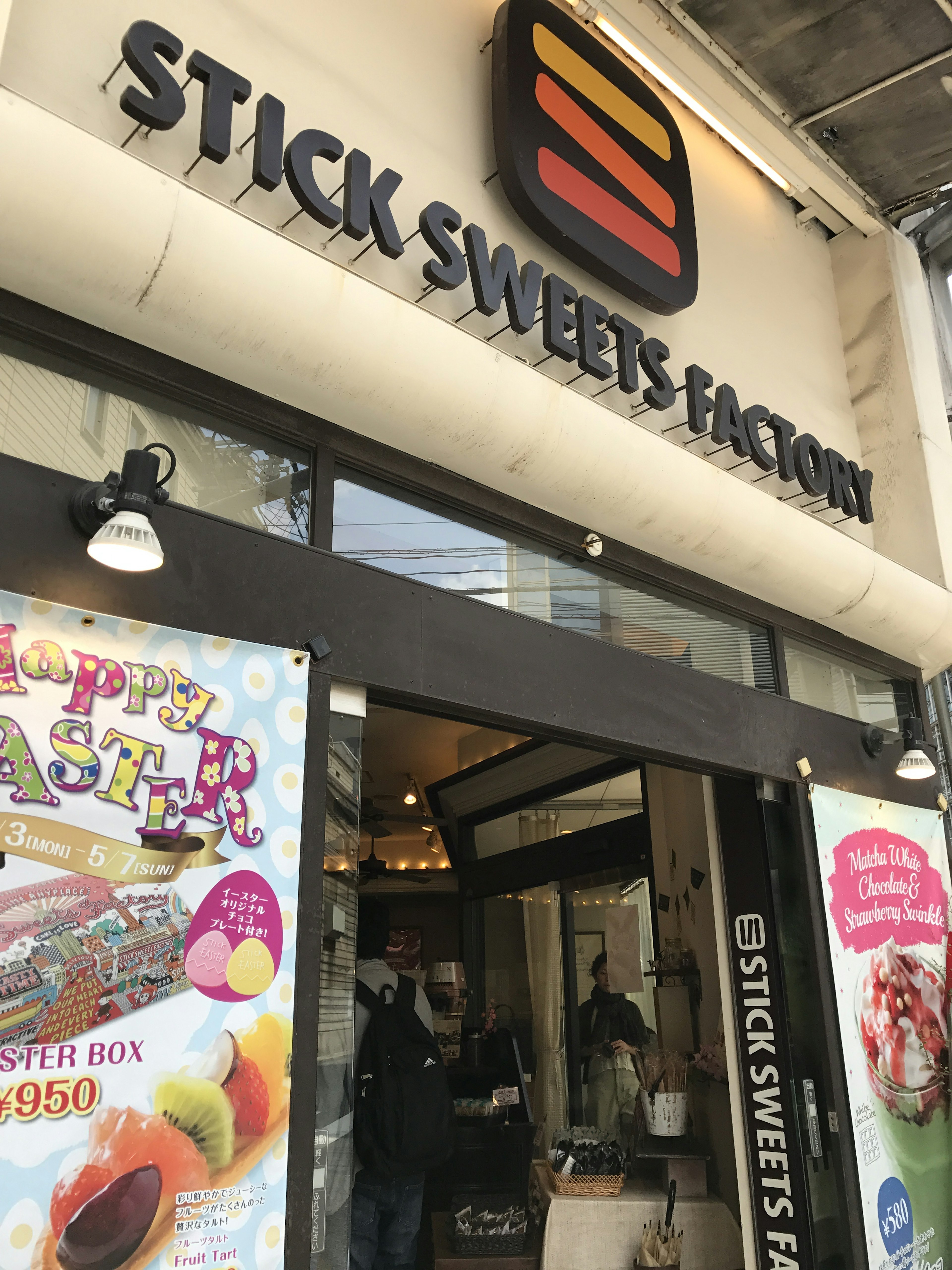 มุมมองภายนอกของ Stick Sweets Factory พร้อมโปสเตอร์สีสันสดใสและป้าย