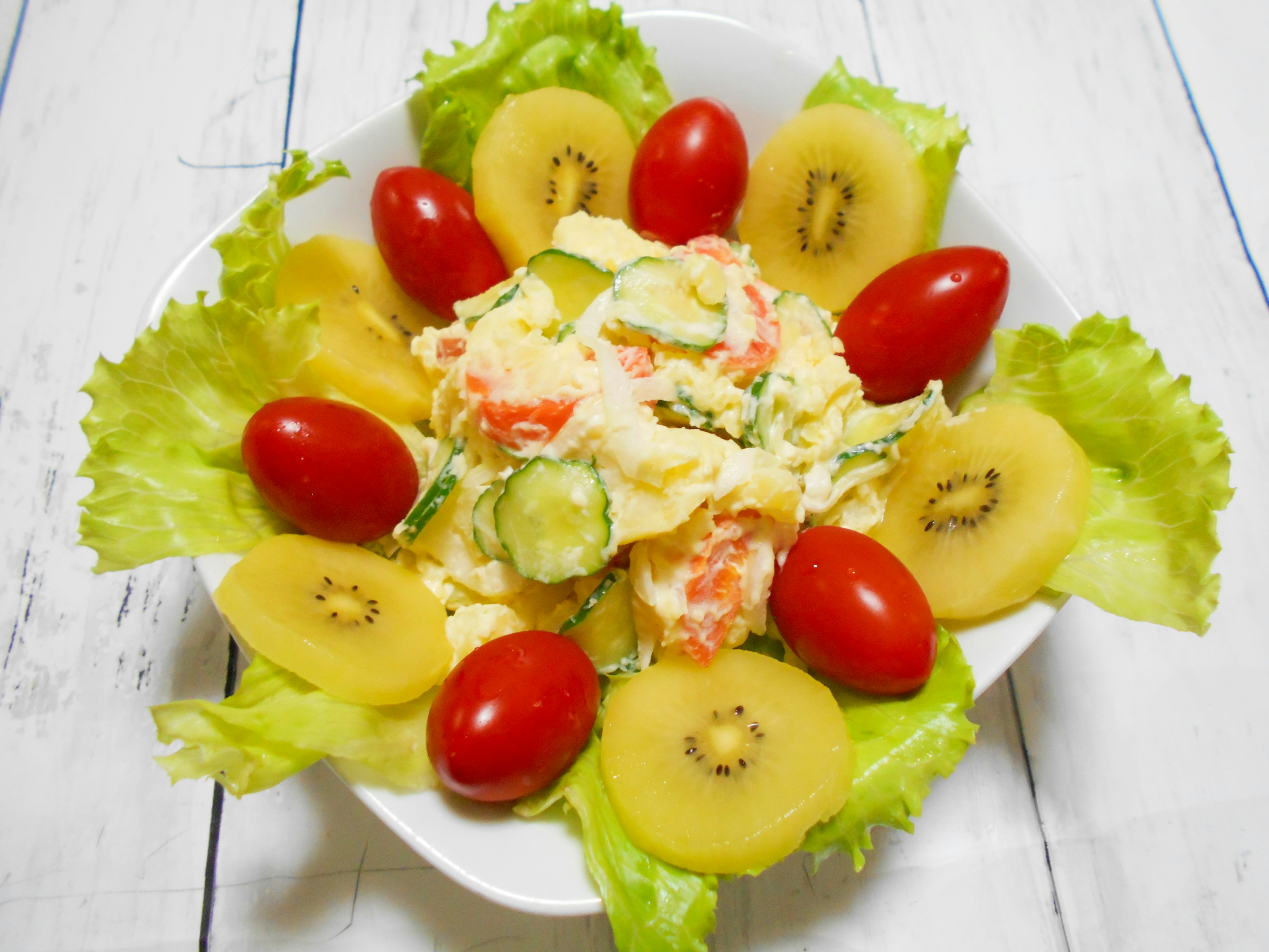 A plate of salad with lettuce, cherry tomatoes, and kiwi arranged decoratively