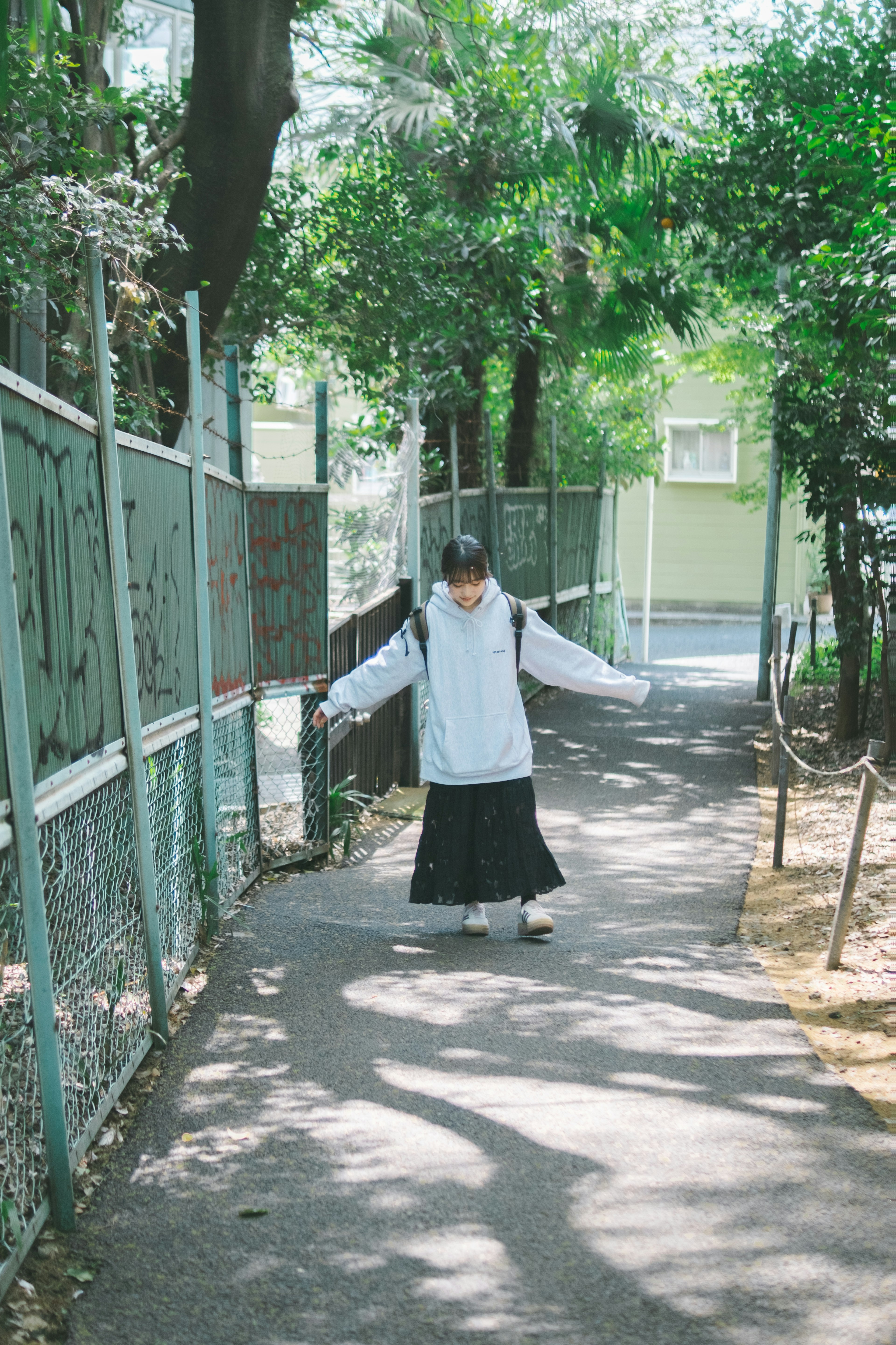 女孩走在绿树环绕的小路上，穿着白色上衣和黑色裙子