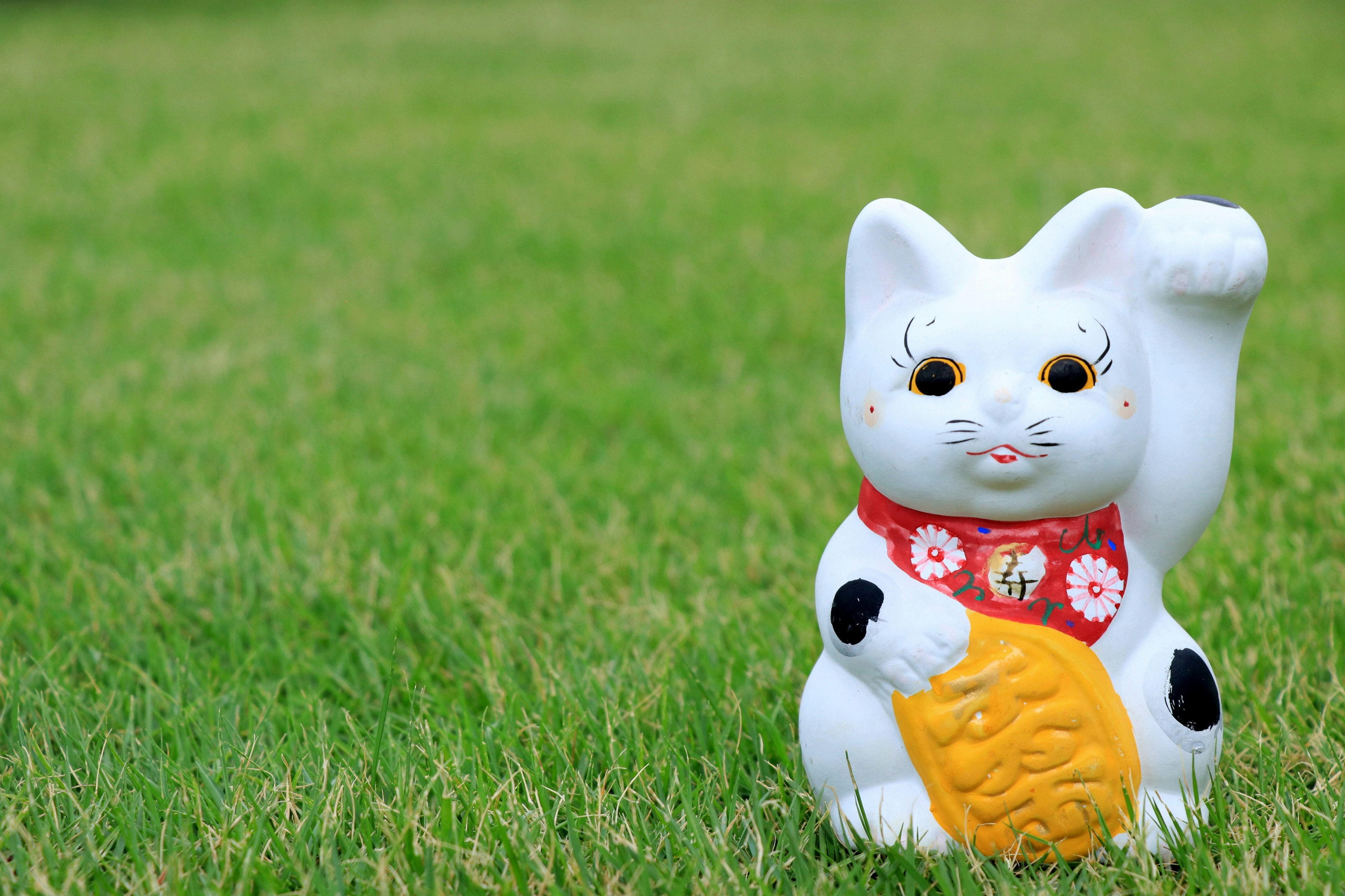 A white cat figurine stands on green grass