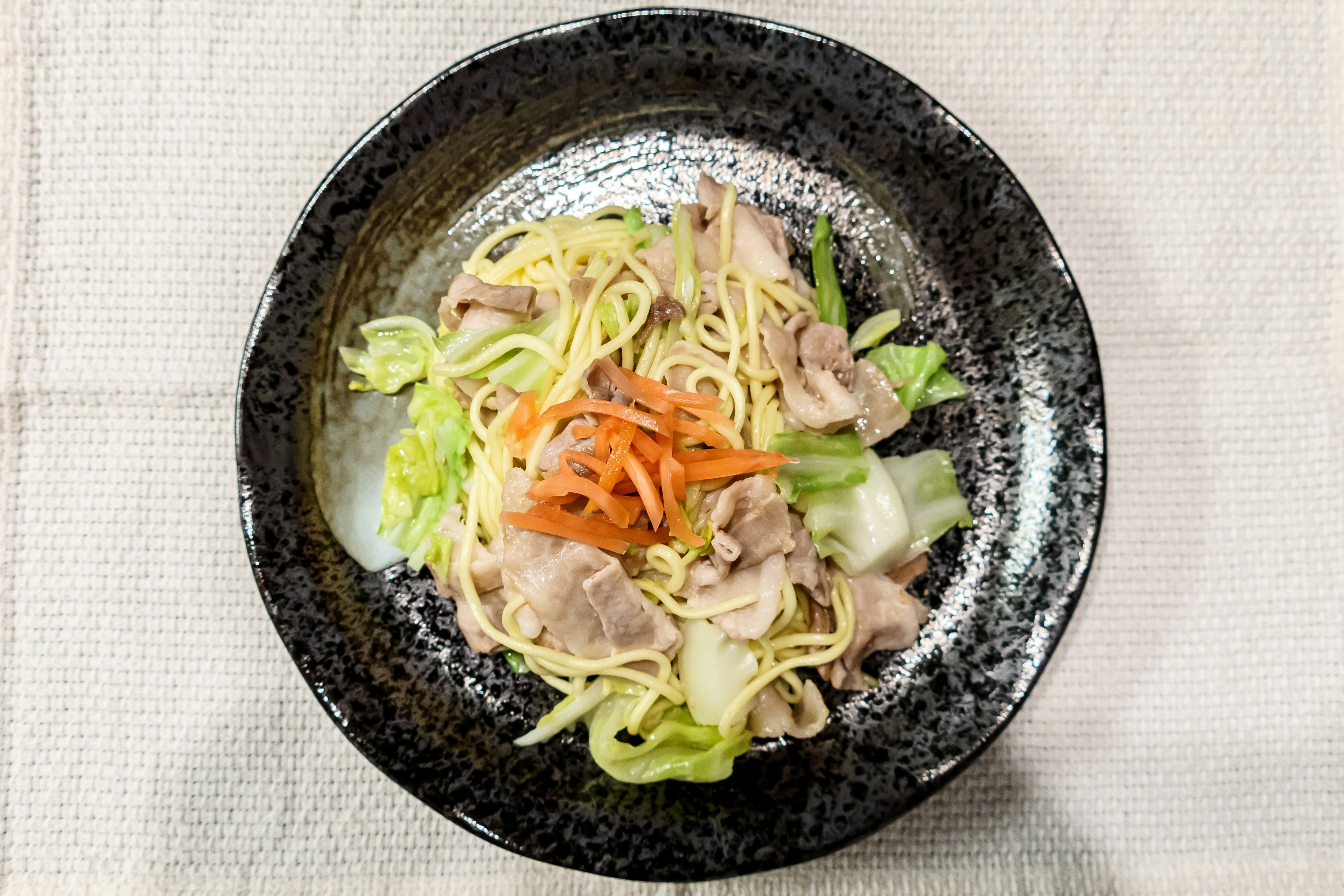 Stir-fried noodles with vegetables and pork served in a black bowl