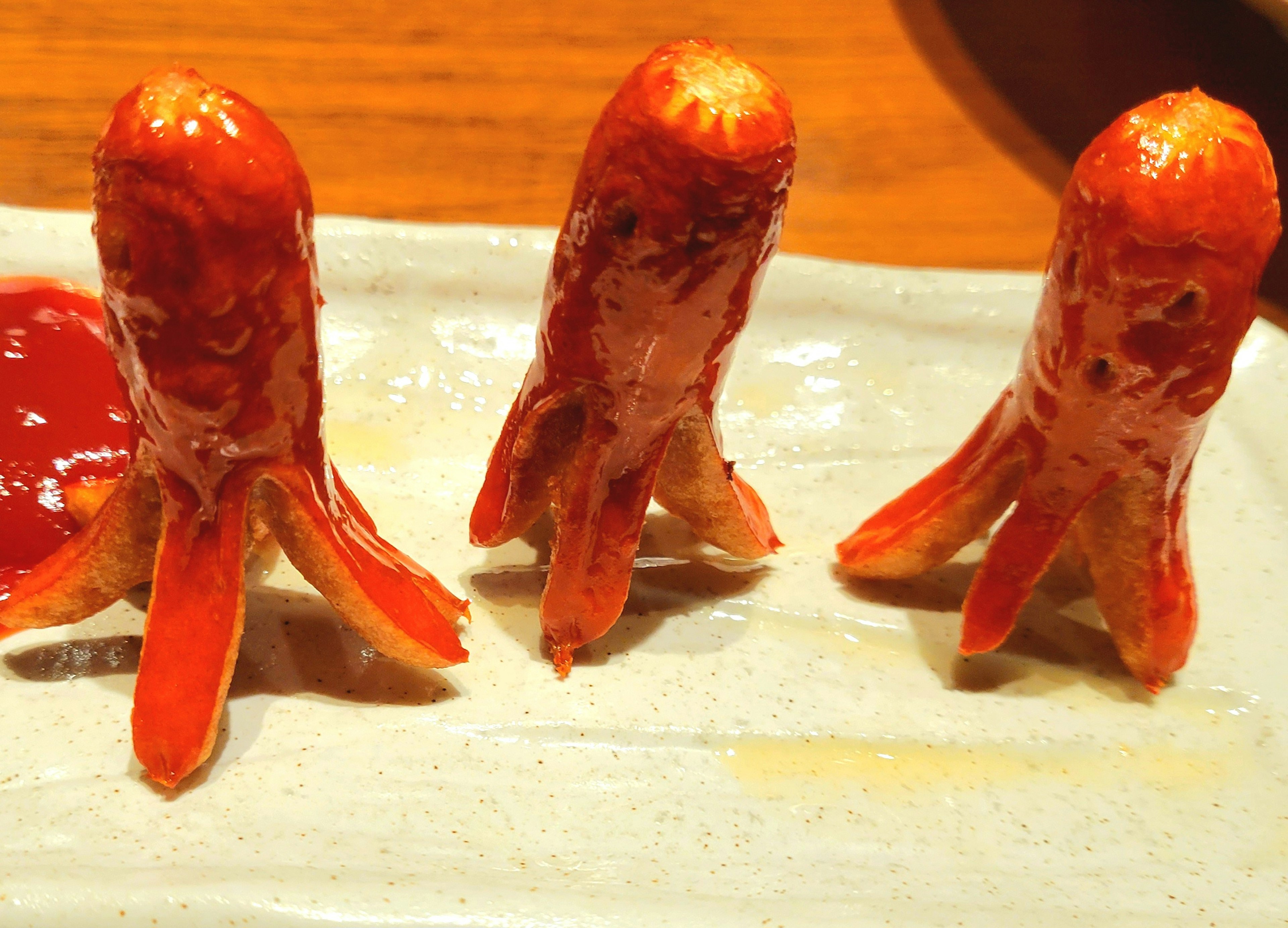 Three red sausages resembling octopuses on a plate