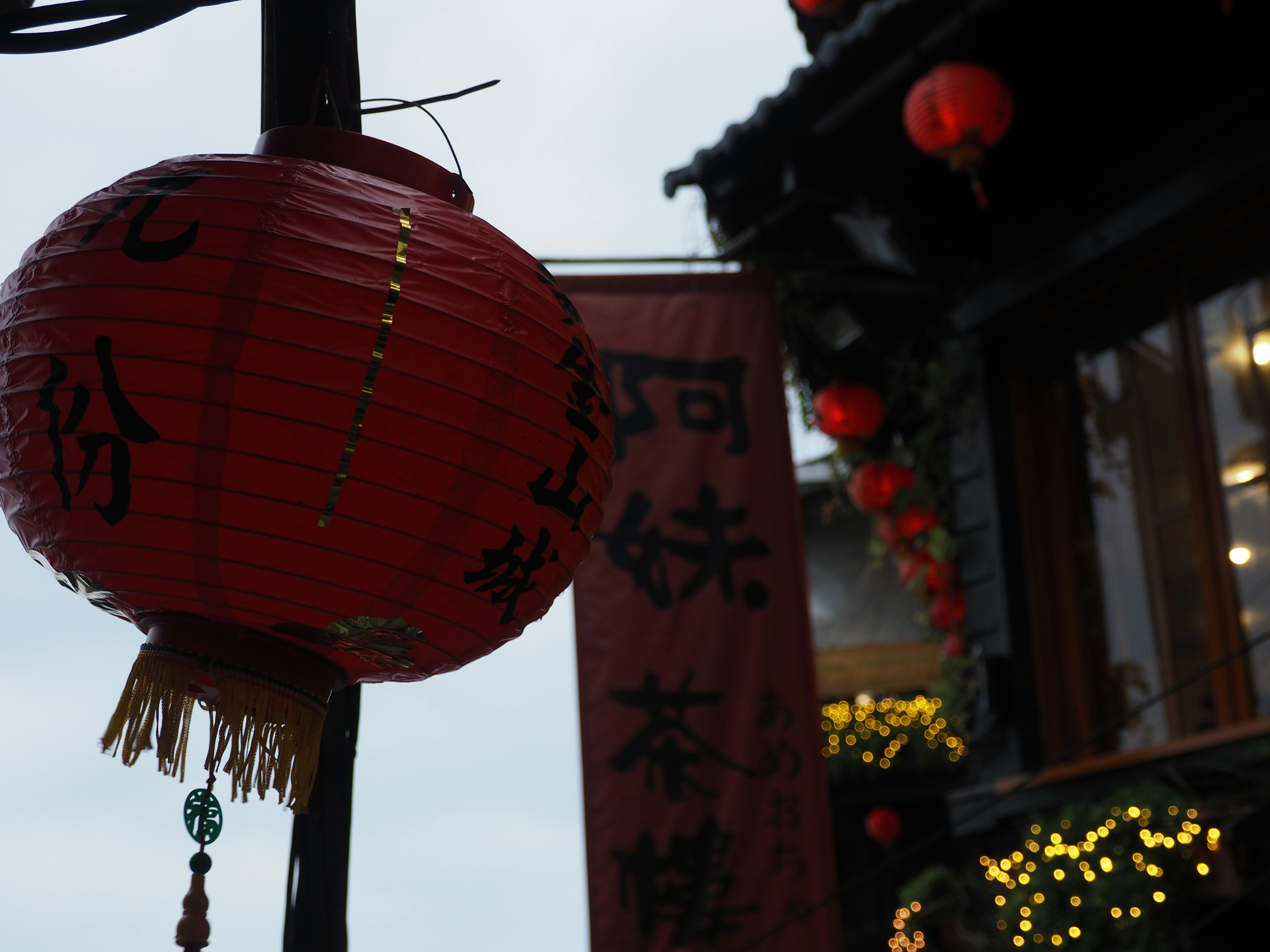 Lampion merah dengan karakter Cina tergantung di samping bangunan tradisional