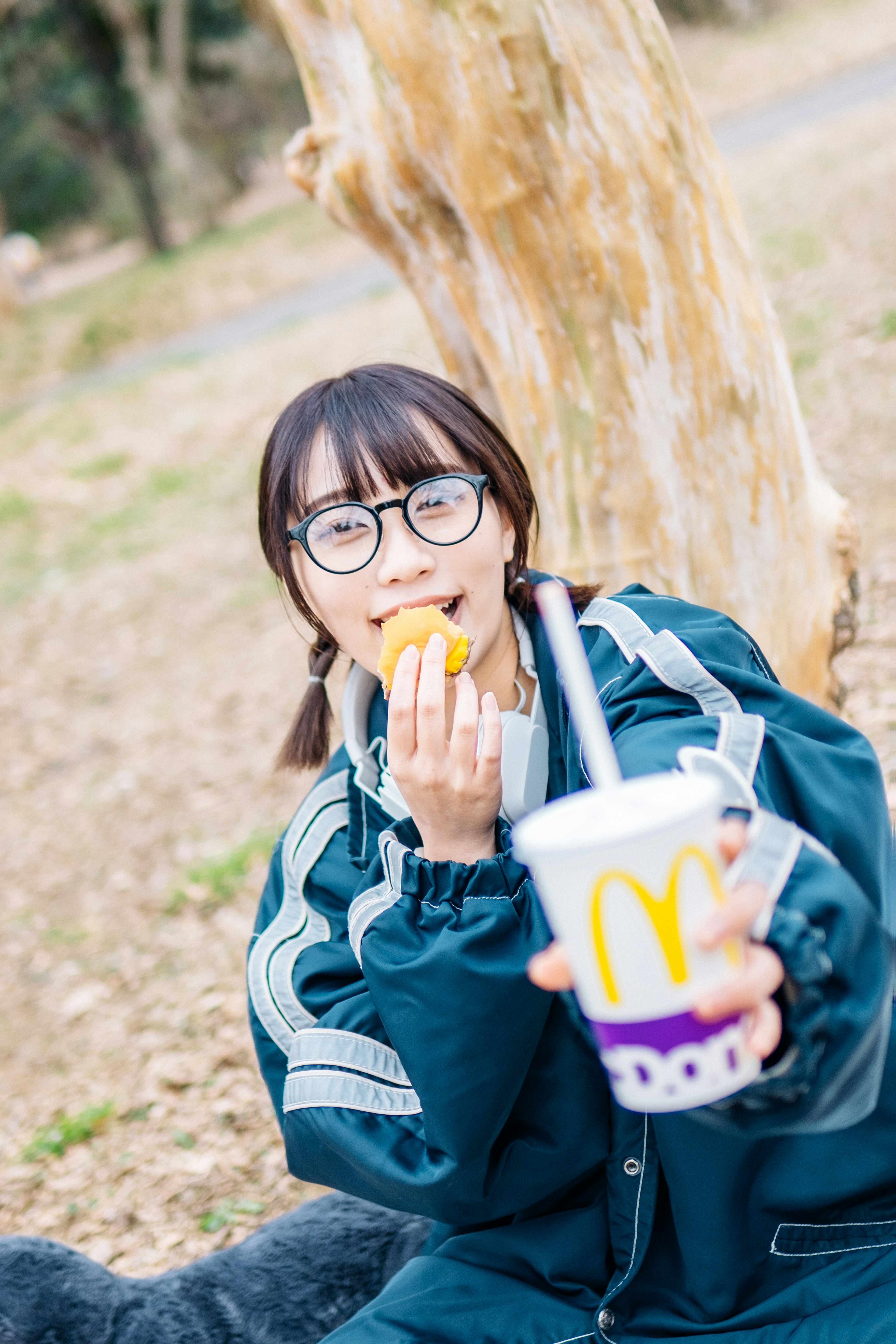 マクドナルドの飲み物を持ち、食べ物を口にしているメガネをかけた女性