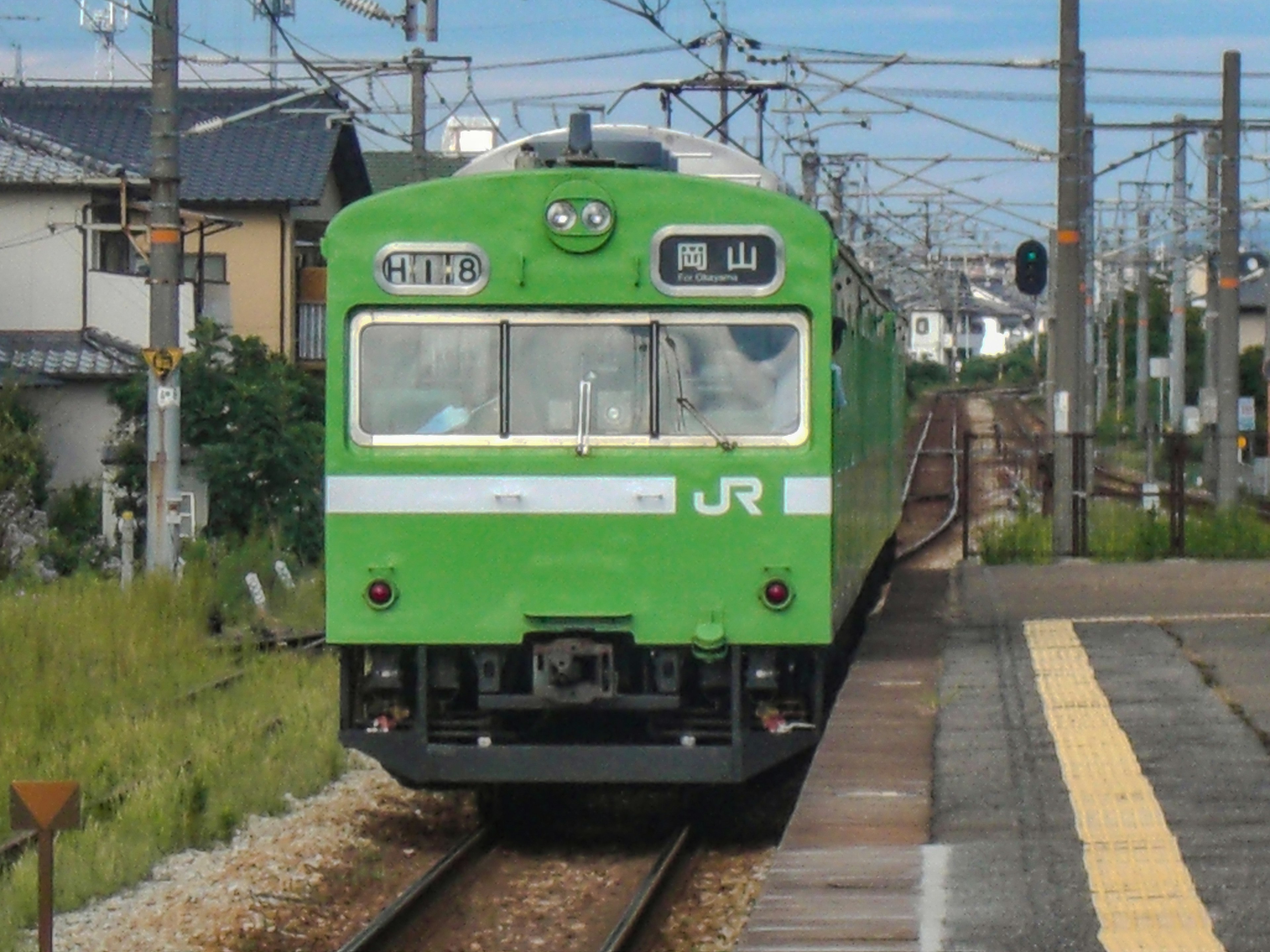 綠色JR列車抵達一個有附近房屋的車站