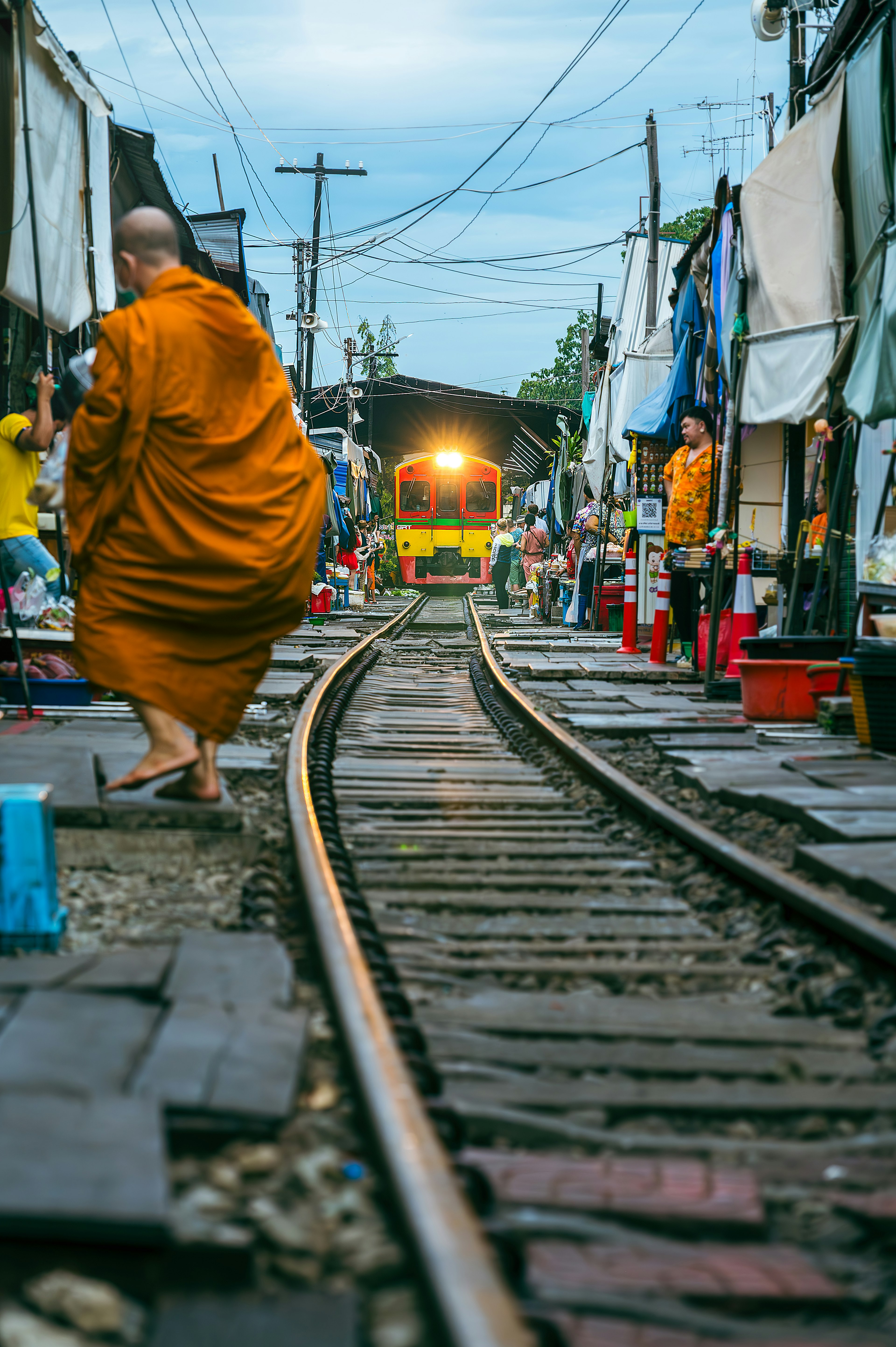 Monks walking along railway tracks with colorful stalls in the evening light