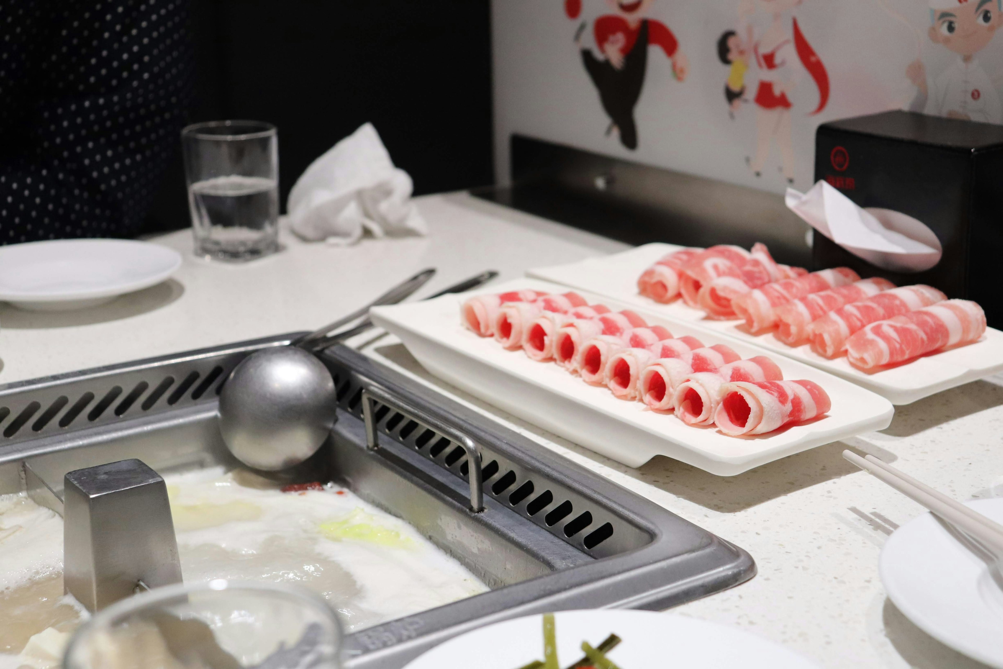 Plates of thinly sliced meat and hot pot setup on a dining table