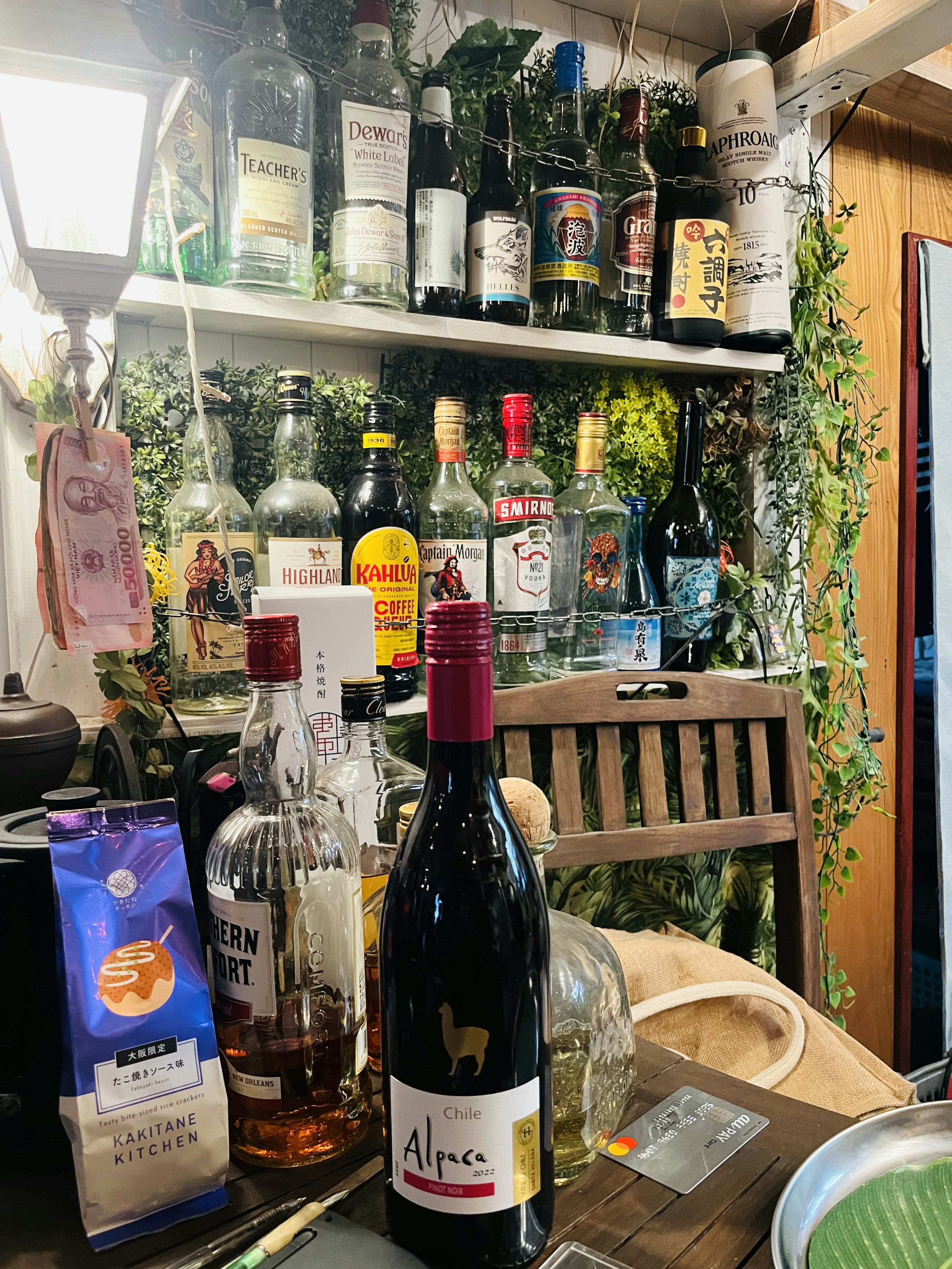 居酒屋のカウンターに並ぶ多様な酒瓶と植物の装飾