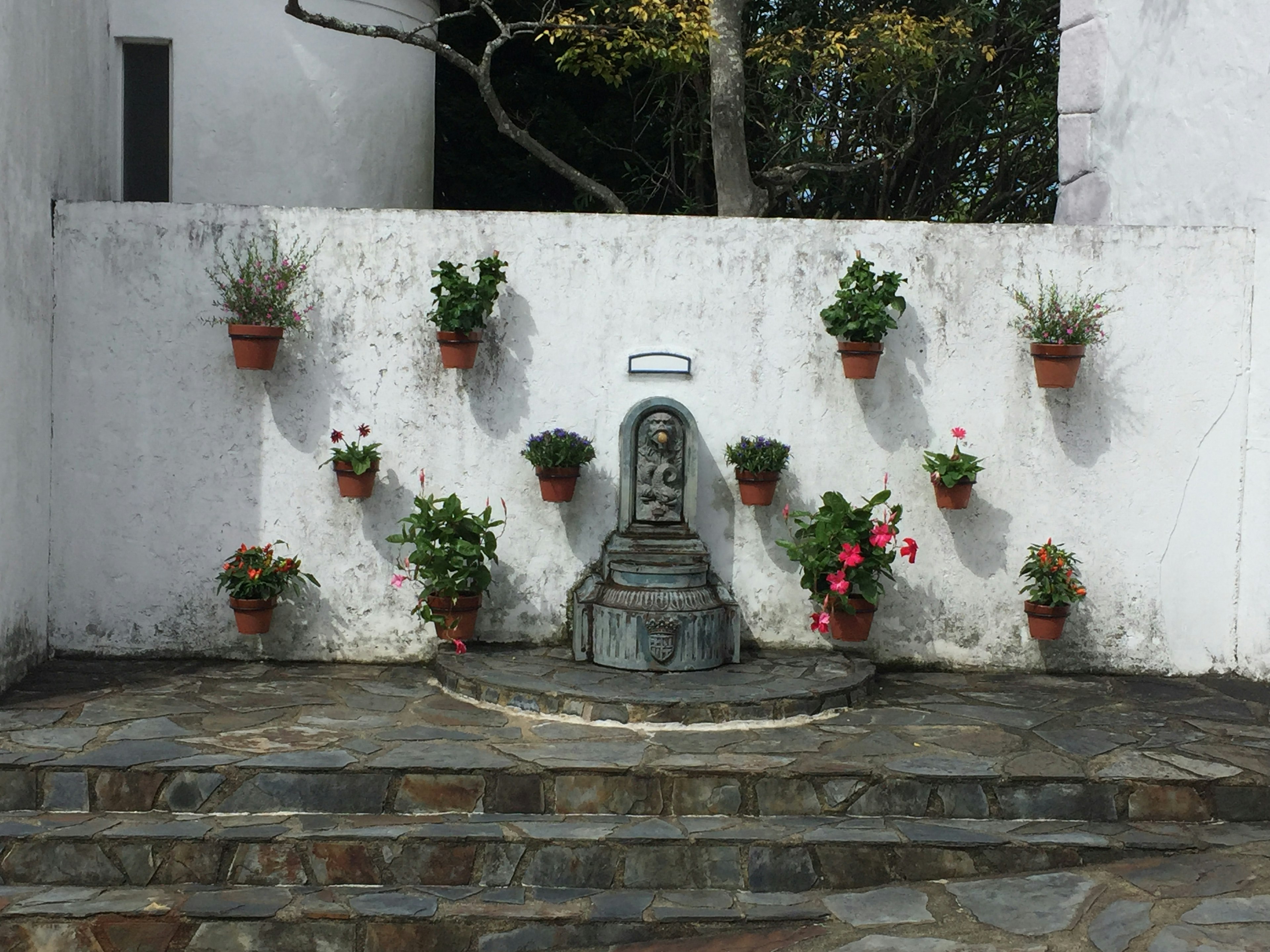 Small garden with a stone statue and flower pots against a white wall